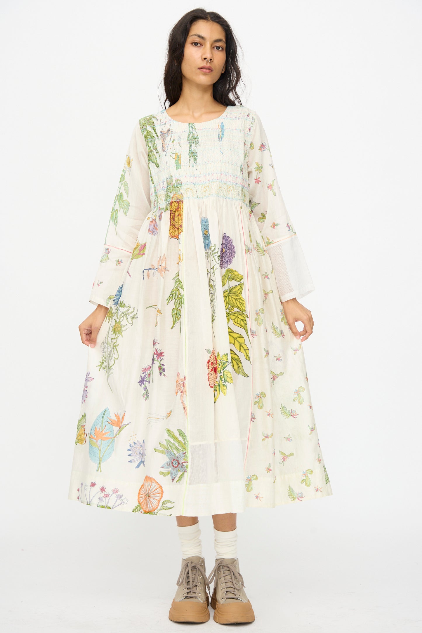 A woman stands facing forward wearing the Injiri Cotton Silk Blockprint Nazma Dress in white, paired with white socks and tan lace-up shoes, set against a plain white background.