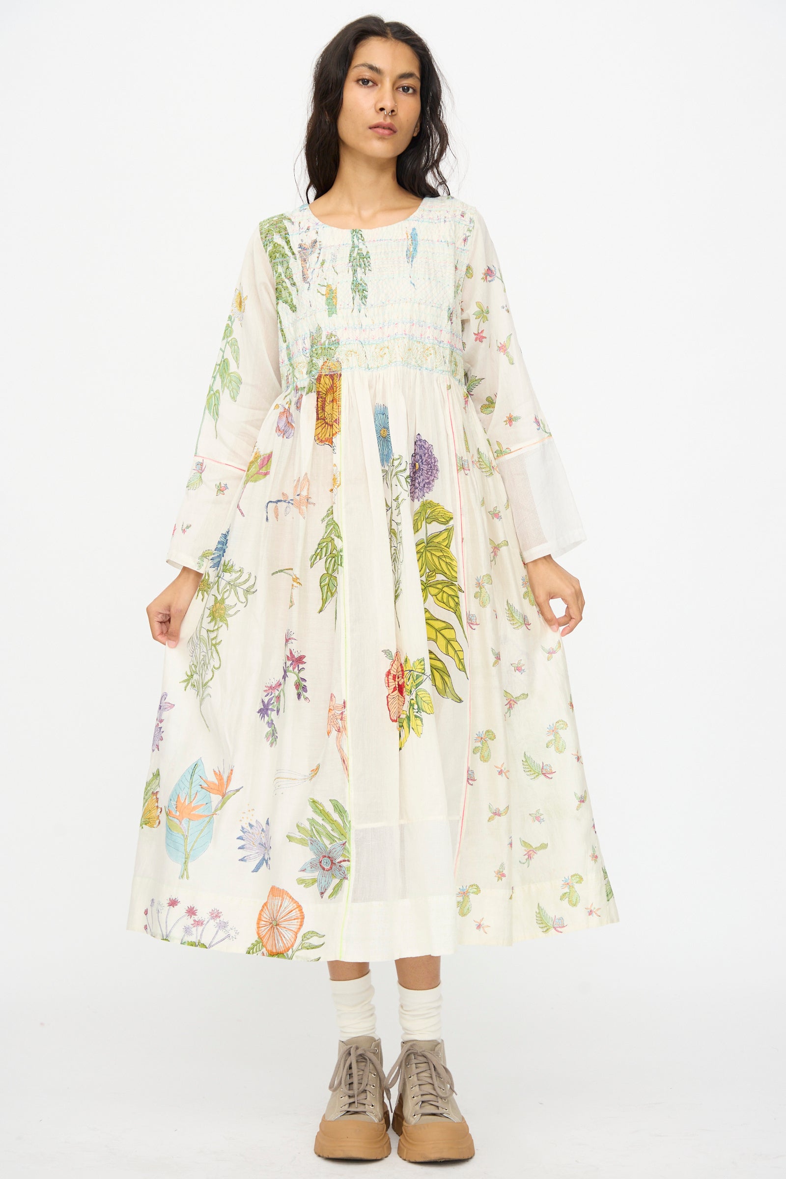 A woman stands facing forward wearing the Injiri Cotton Silk Blockprint Nazma Dress in white, paired with white socks and tan lace-up shoes, set against a plain white background.