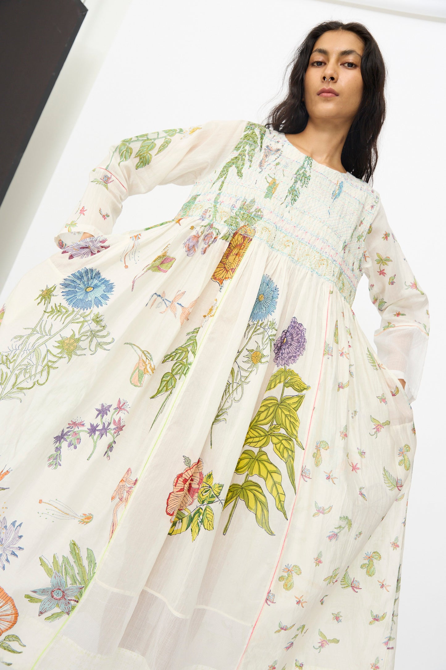 A woman wears the Cotton Silk Blockprint Nazma Dress in White by Injiri, standing with her hands holding the sides of the dress and looking down at the camera.