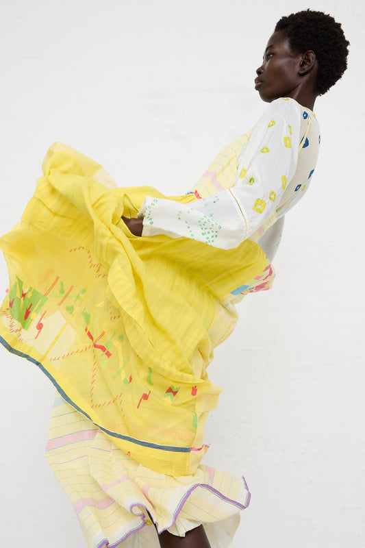 A woman with short hair in a dynamic pose wearing an Injiri Cotton Slip Dress in Yellow with colorful embroidered details against a white backdrop.
