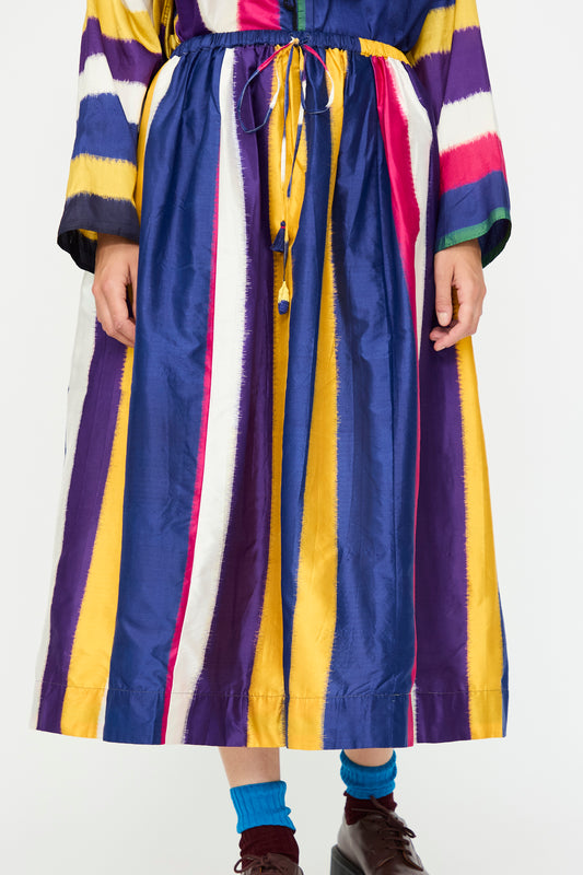 A person wearing the Injiri Ikat Silk Skirt lined with Cotton in Multi Stripe, paired with blue socks and burgundy shoes.