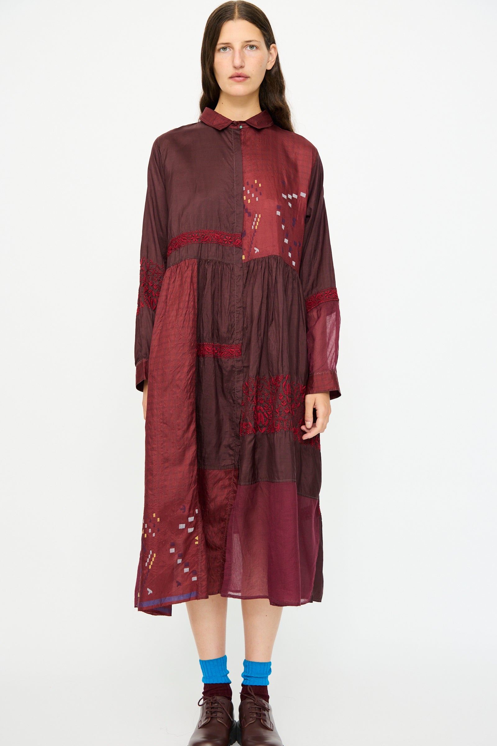 A woman stands against a white background wearing the Injiri Silk and Cotton Dress in Red, styled with brown shoes and blue socks.