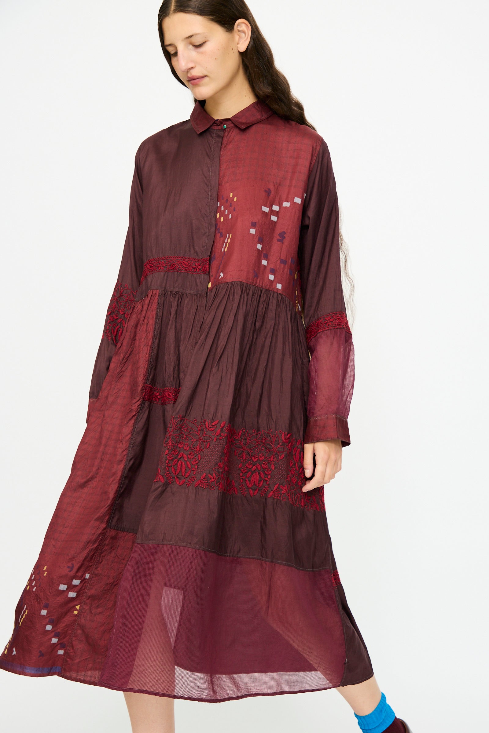 A woman wears the Injiri Silk and Cotton Dress in Red, featuring long sleeves and embroidered details, standing against a plain white background.