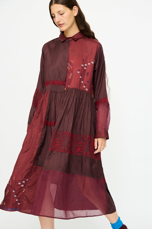 A woman wears the Injiri Silk and Cotton Dress in Red, featuring long sleeves and embroidered details, standing against a plain white background.