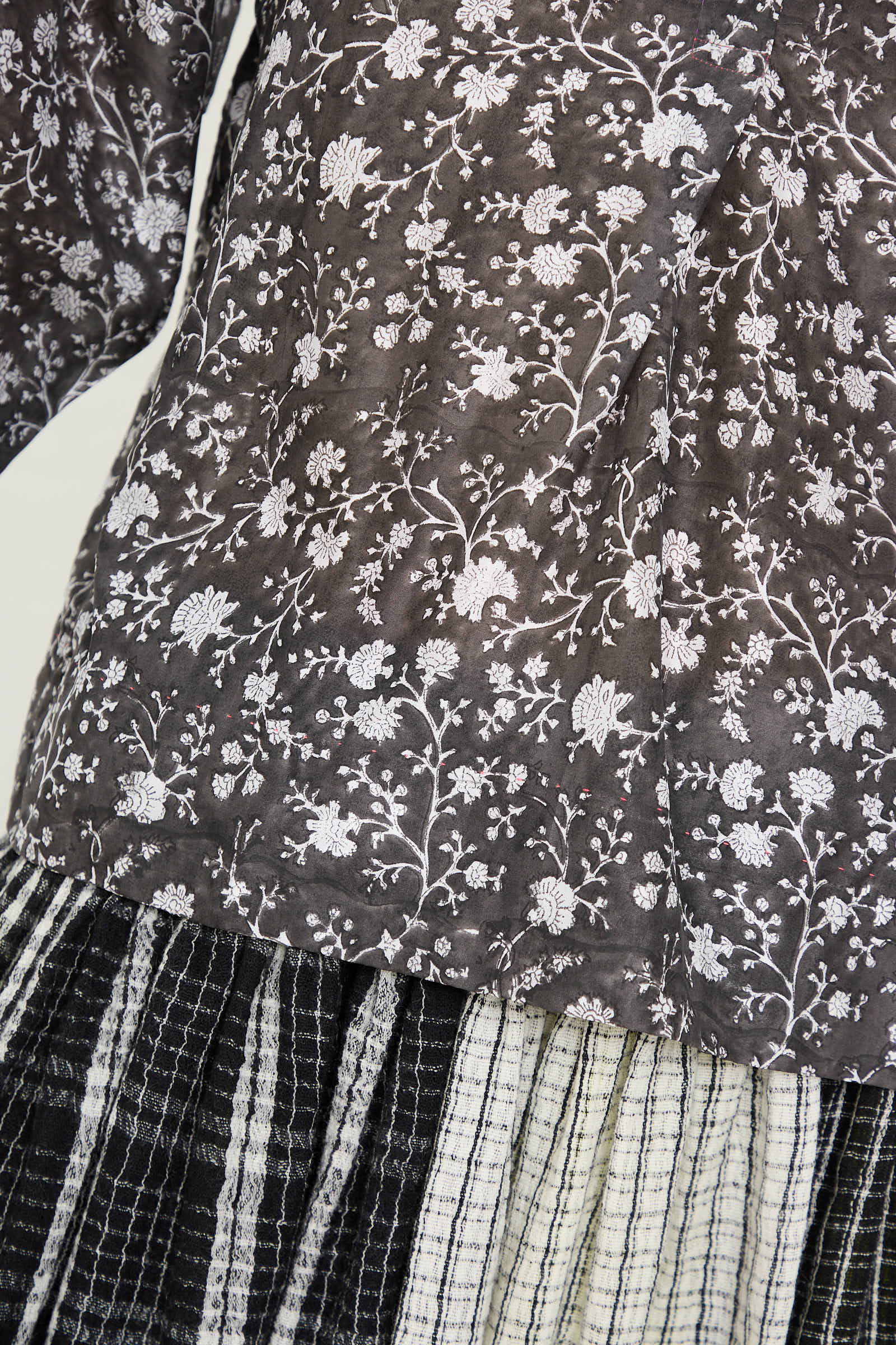 Close-up of a person wearing the Silk Blouse in Floral Print by Injiri, paired with a pleated skirt featuring black, white, and gray stripes.