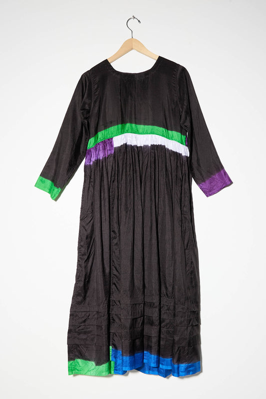 A long-sleeved Silk Dress in Black, Purple, and Green with horizontal green, purple, white, and blue stripes on the sleeves and lower tiered skirt by Injiri, displayed on a wooden hanger.