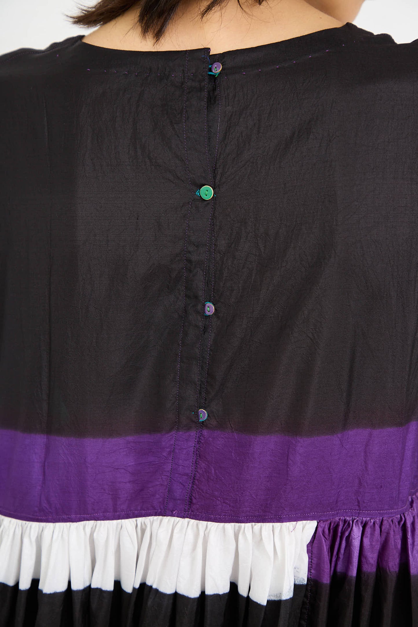 Close-up view of the back of the Injiri Silk Dress in Black, Purple, and Green featuring a black top part with center buttons, a purple midsection, and a white lower section with gathered fabric, offering colorful pops that enliven this stunning piece.