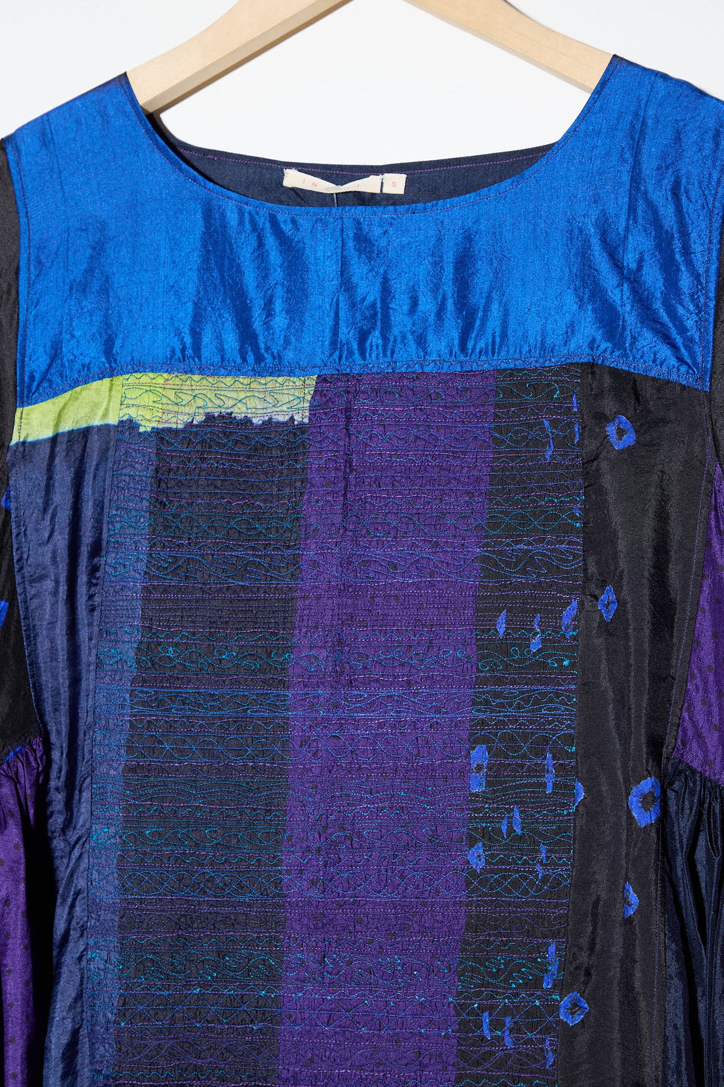 Close-up of the Injiri Silk Dress in Purple, Black and Blue. This long sleeve dress features a blue neckline and fabric in various shades of blue, purple, and black with textured patterns and a patchwork design. A hanger is visible at the top.