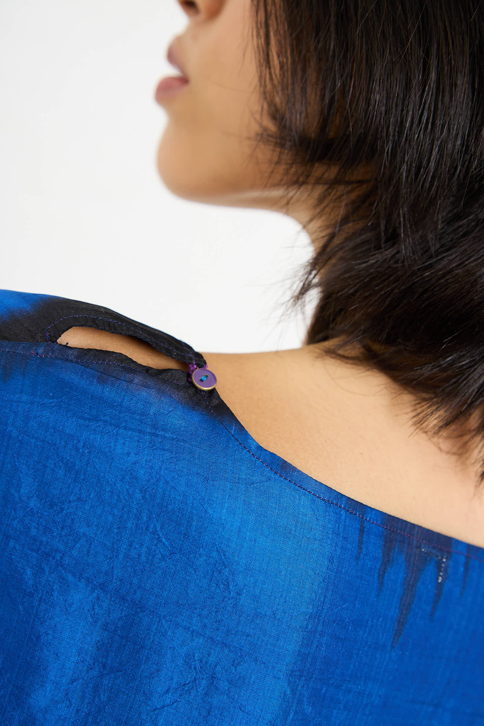 Close-up of a person wearing the Injiri Silk Dress in Blue, showing the back neckline with two buttoned fastenings. The person's hair is short and partially covers one side of their face.