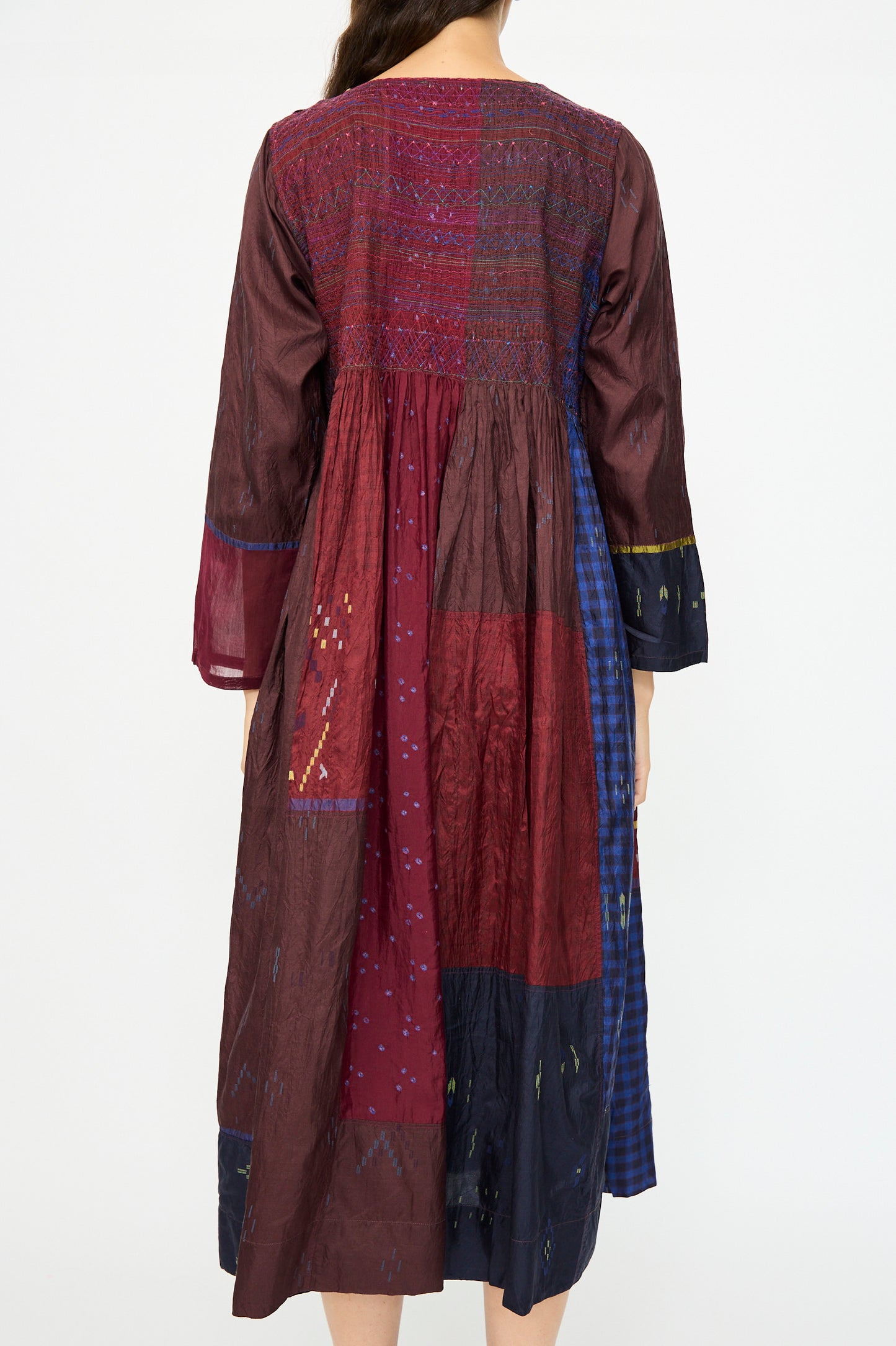 A person shown from behind wears the Injiri Silk Dress in Red and Blue Multi, a long-sleeve, ankle-length hand-dyed silk dress featuring a multicolored patchwork design.