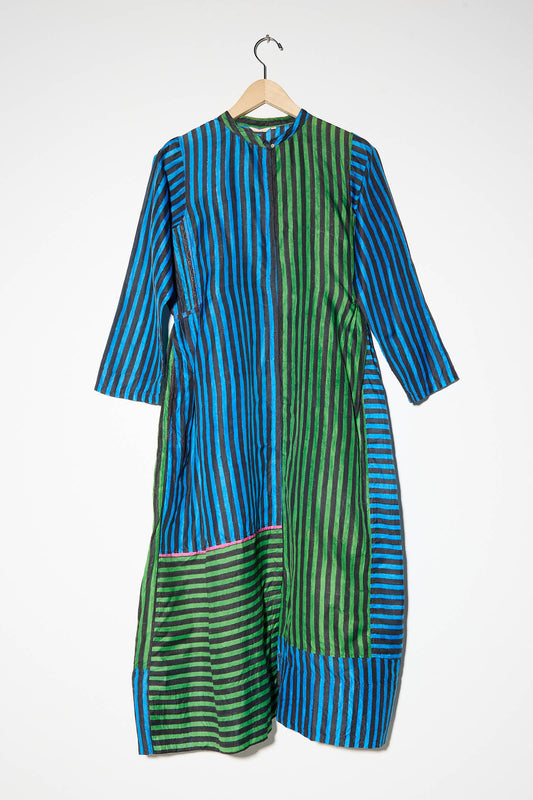 The Injiri Silk Dress in Stripe Blue and Green is a long-sleeved dress with a collar, showcasing intricate stitch design and vertical stripes in varying widths of blue and green. It is elegantly hung on a wooden hanger against a plain white background.