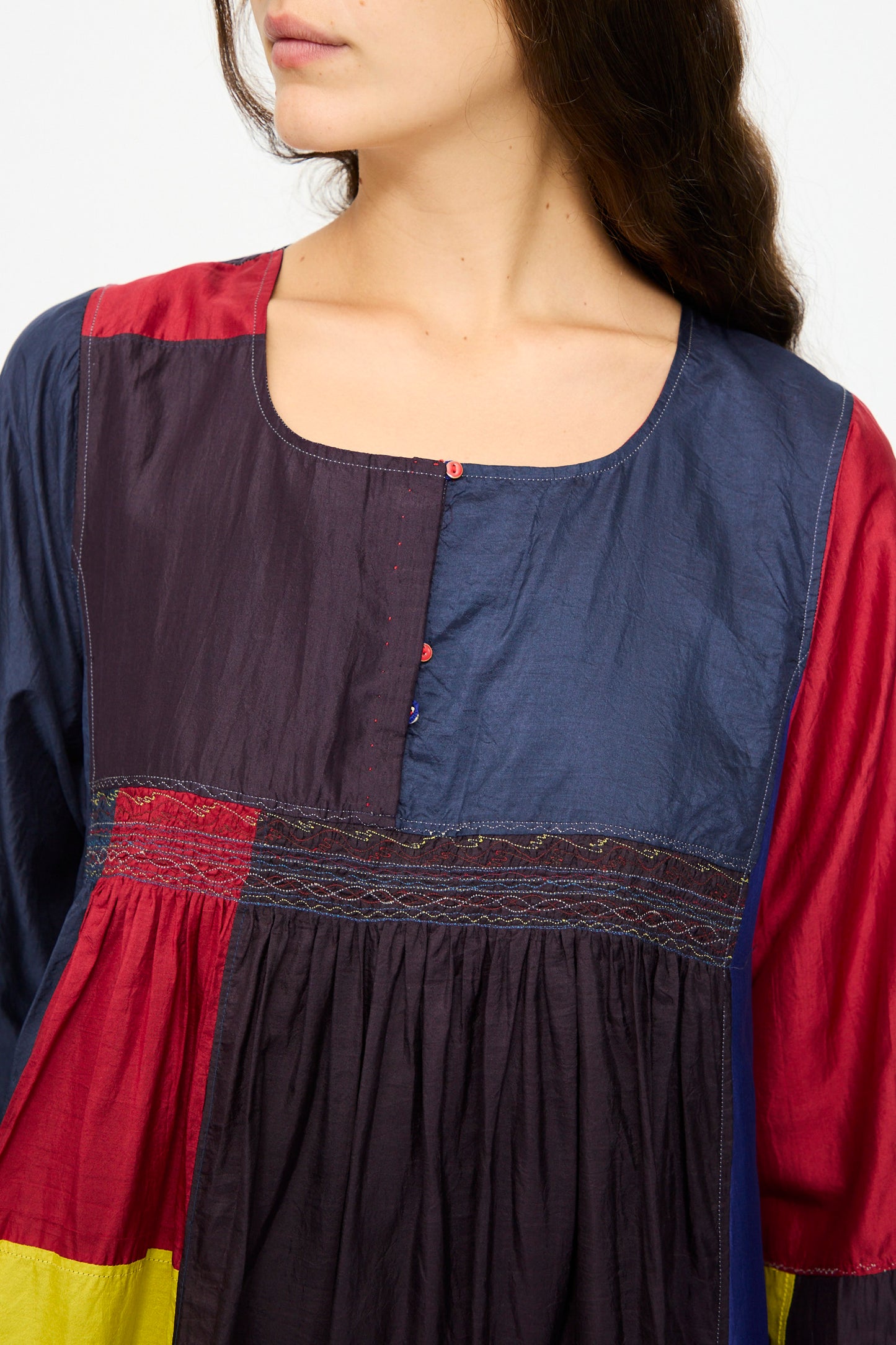 A woman in the Injiri Silk Dress in Red, Blue and Yellow Multi, featuring a relaxed fit, long sleeves, a square neckline, and gathered fabric detail is photographed from shoulders to mid-torso.