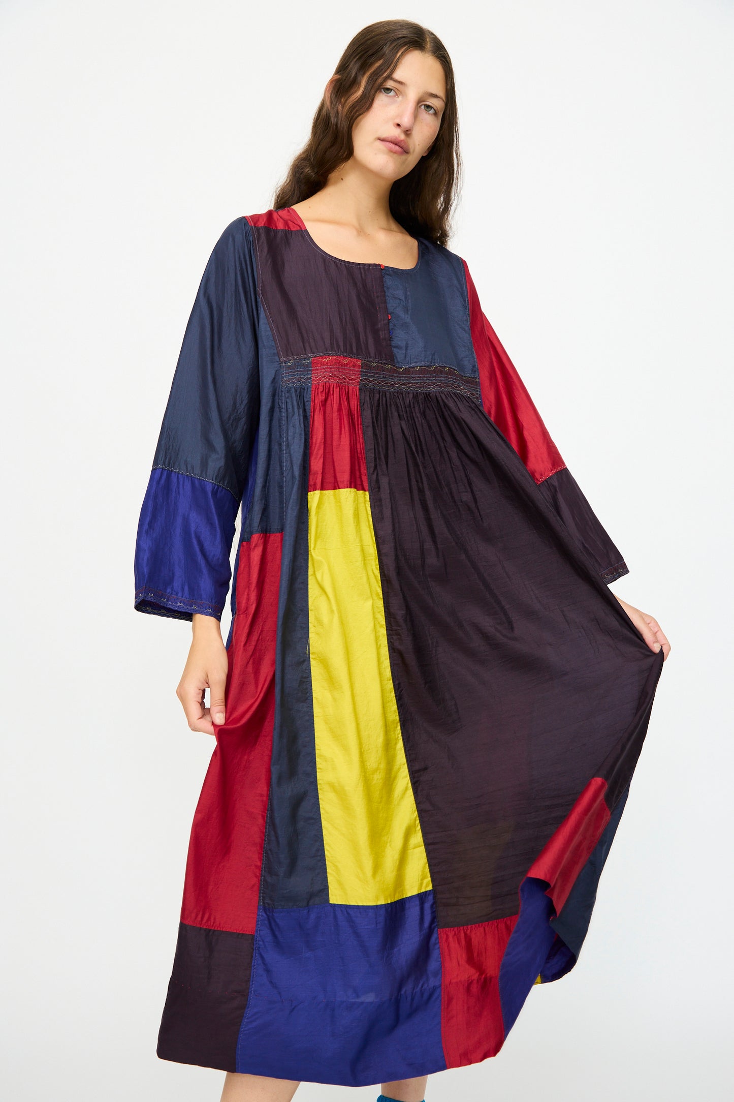 A woman stands against a white background wearing the Injiri Silk Dress in Red, Blue and Yellow Multi, a relaxed fit long-sleeve dress with bold color blocks.