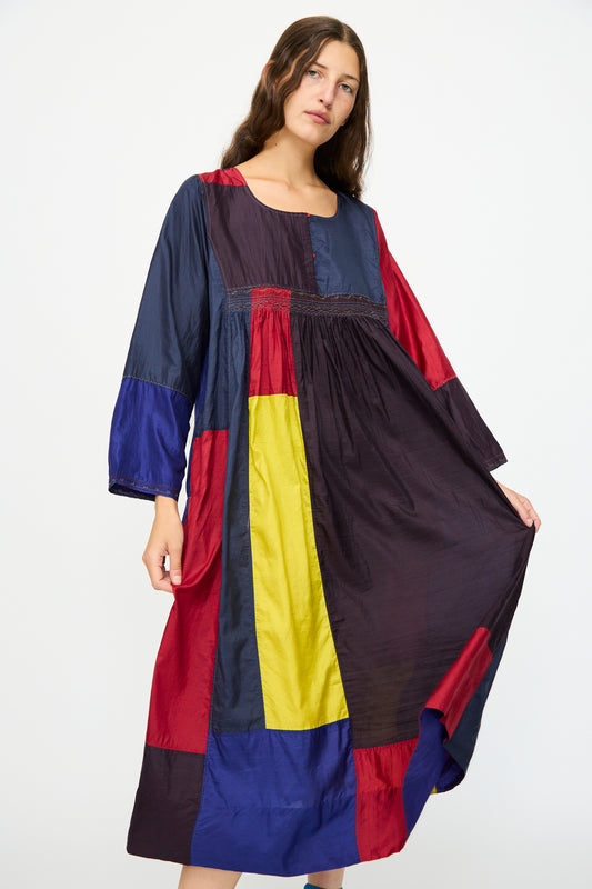 A woman stands against a white background wearing the Injiri Silk Dress in Red, Blue and Yellow Multi, a relaxed fit long-sleeve dress with bold color blocks.