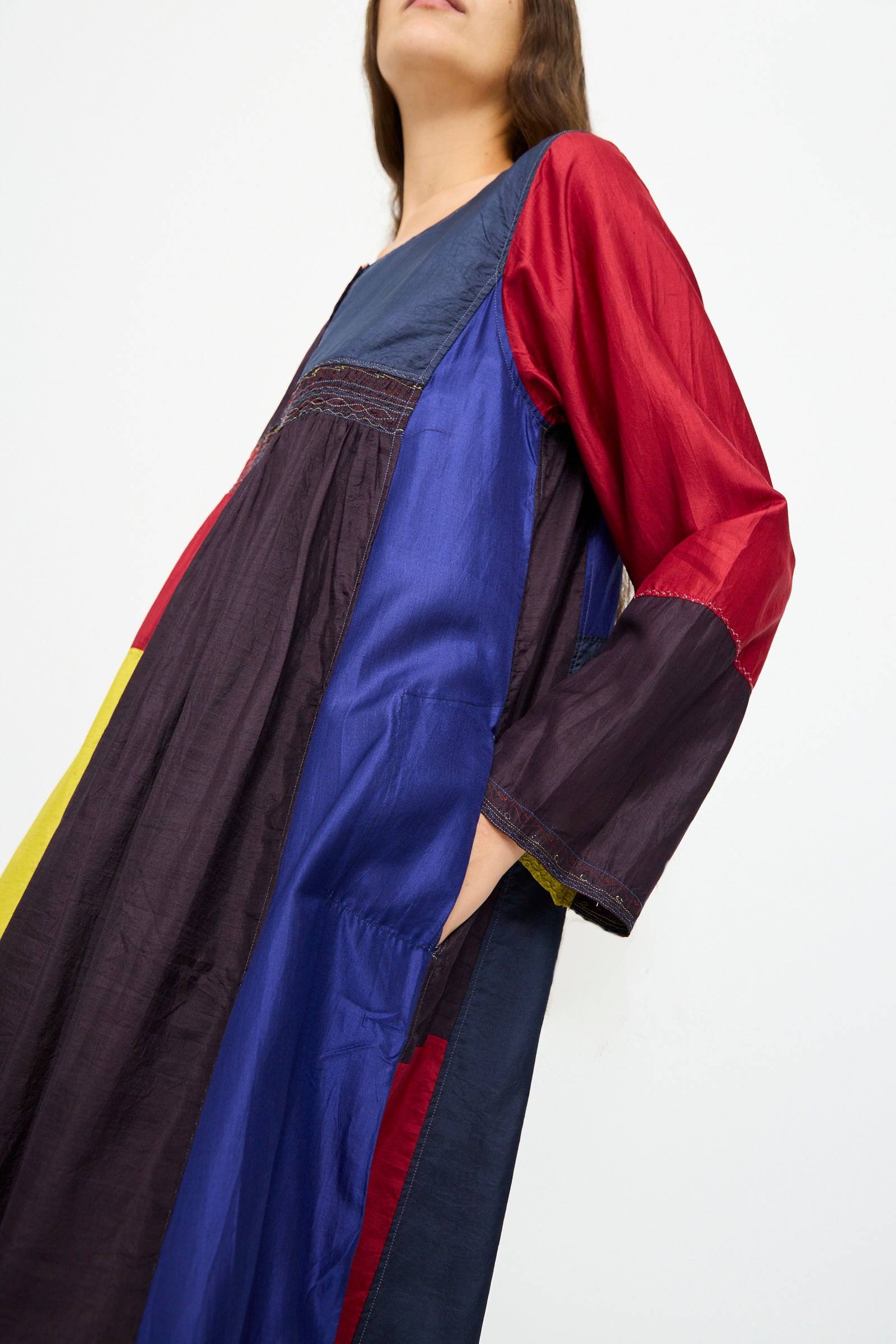 A woman stands against a plain background wearing the Injiri Silk Dress in Red, Blue and Yellow Multi—a relaxed fit, long-sleeve color-blocked design.