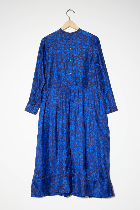 The Silk Floral Print Dress in Blue by Injiri, which is long-sleeved and ankle-length, hangs on a wooden hanger against a plain white background.