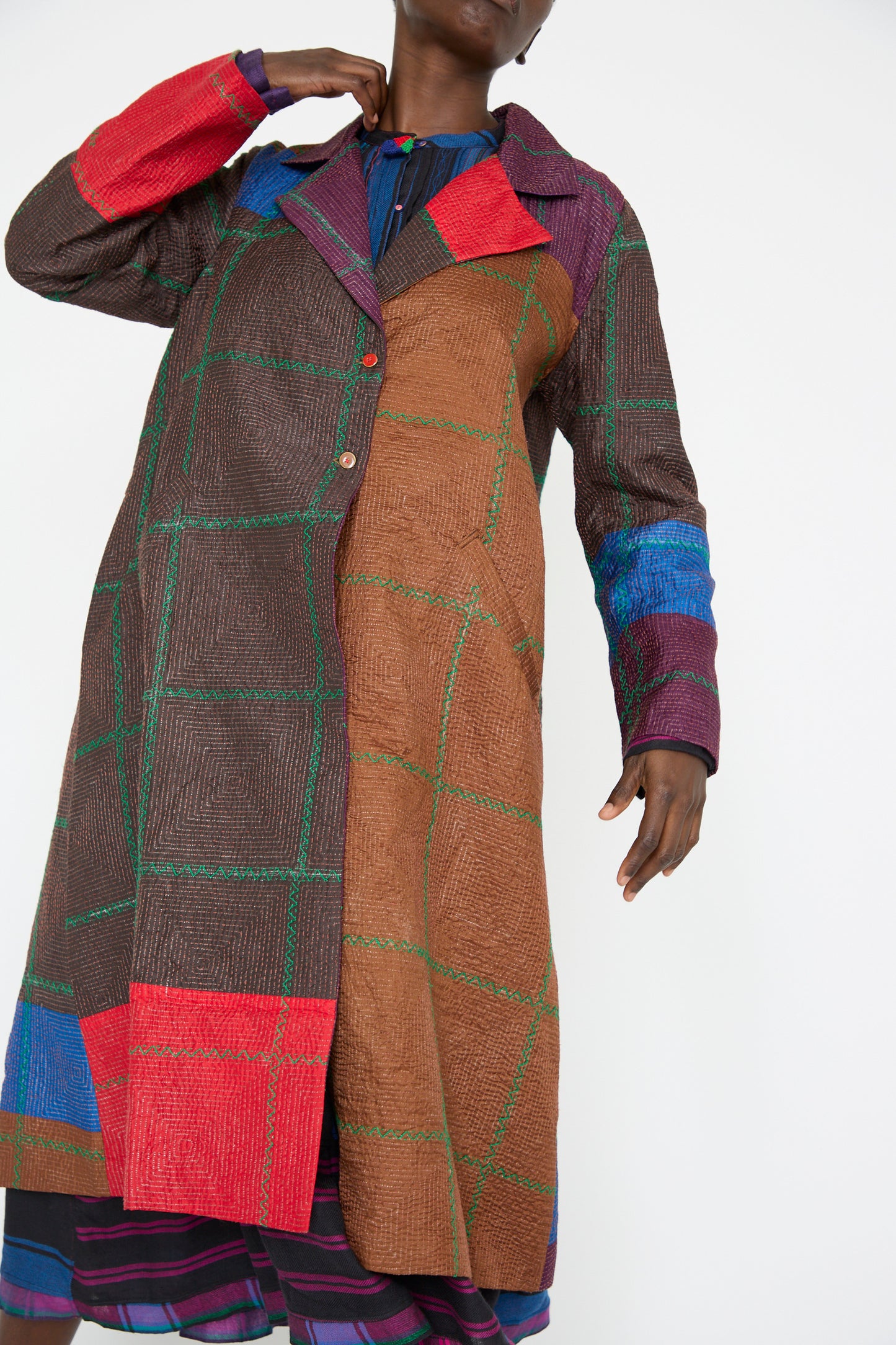 A person wearing the "Silk Jacket in Brown and Multi" by Injiri, featuring a colorful patchwork pattern with block embroidery on its long sleeves and collar, set against a plain background.