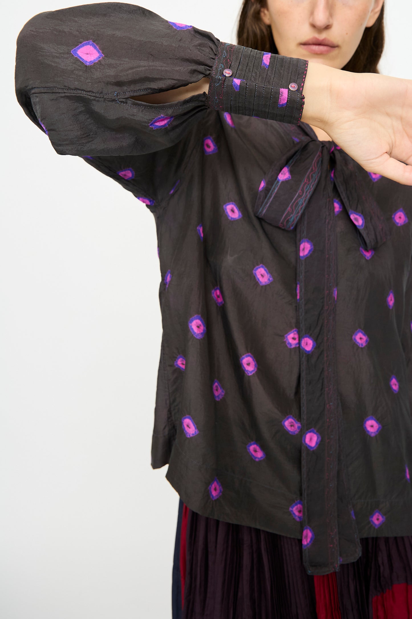 Someone wearing the Injiri Silk Shirt in Purple, which features purple and pink geometric patterns, covers part of their face with their arm.
