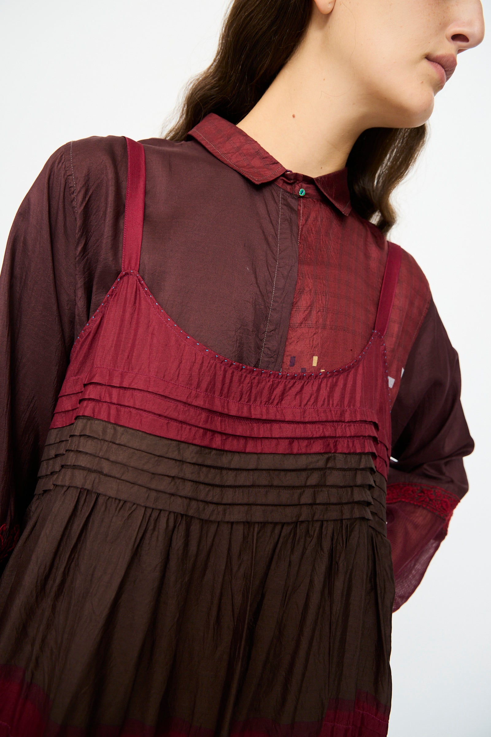 A person wears the Silk and Cotton Slip Dress in Red by Injiri, layered over a burgundy collared shirt.
