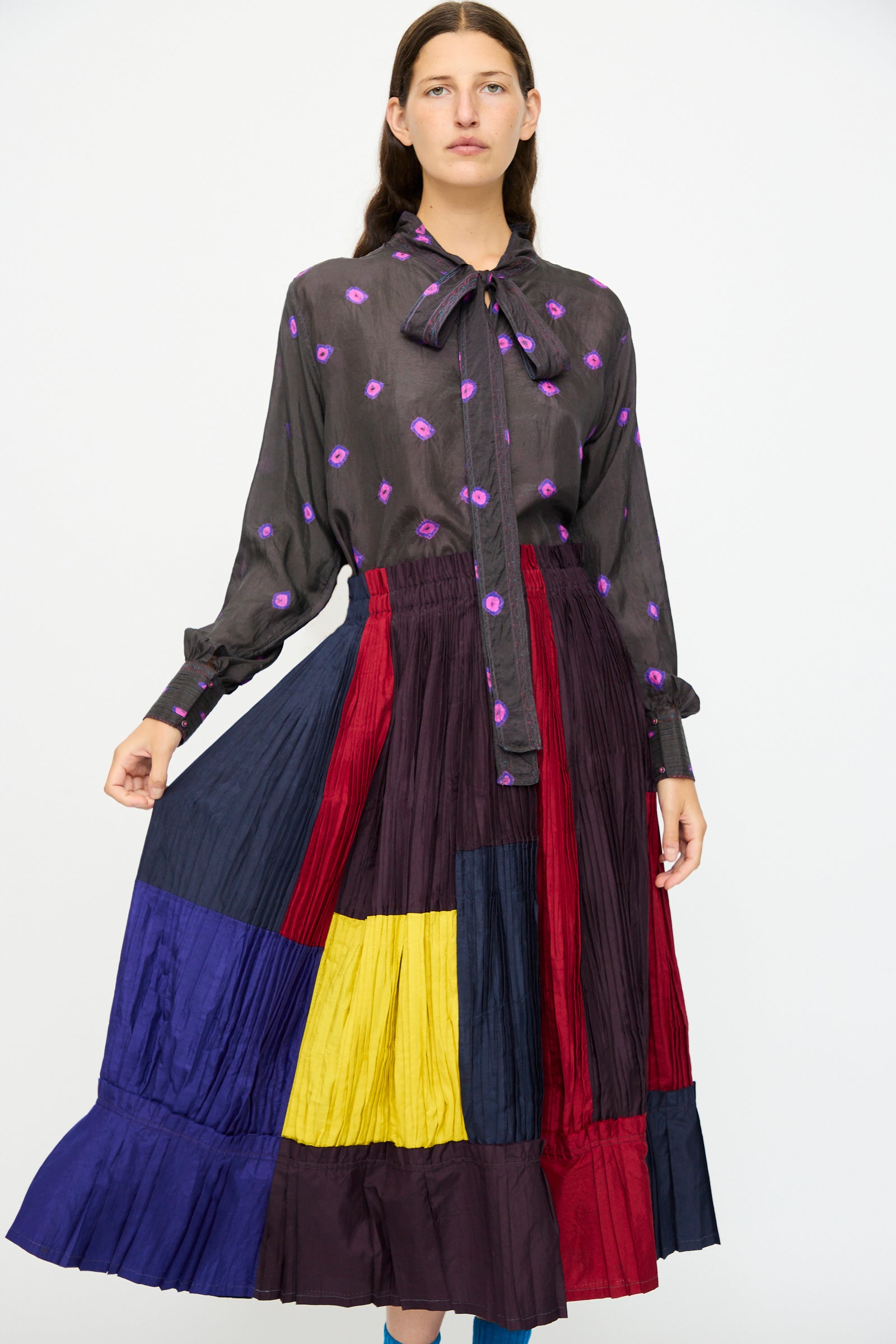 A woman wears a sheer black blouse with purple floral patterns and a necktie, paired with the Injiri Taffeta Silk Skirt in Multi.