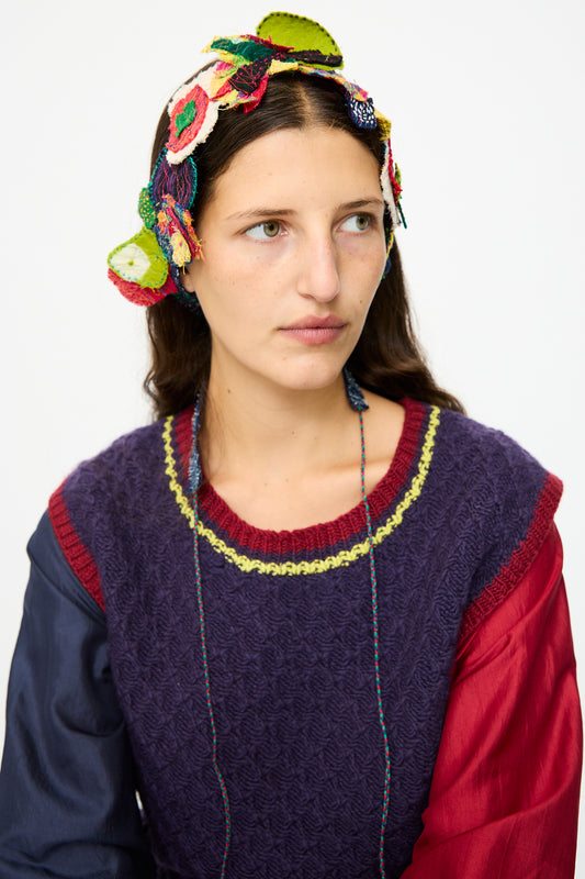 A woman with long brown hair wears the Injiri Wool and Cotton Belt in Multi, styled over a textured purple sweater with red floral sleeves, looking slightly to the side against a plain white background.