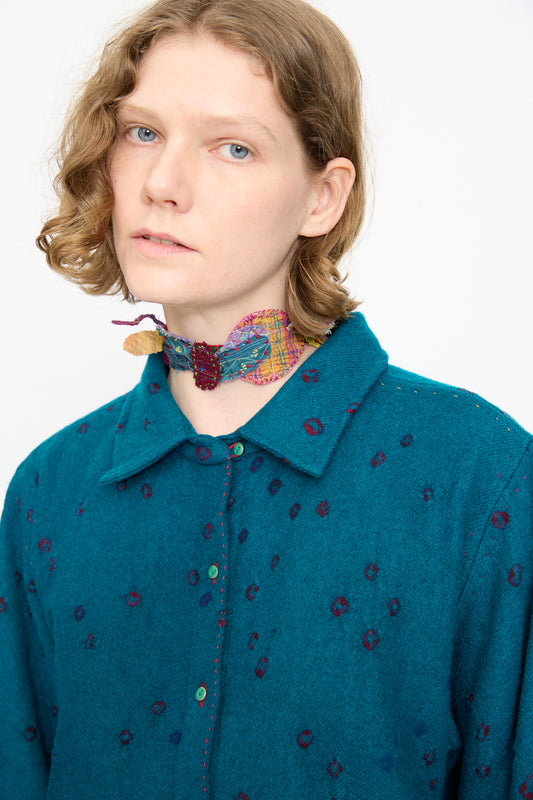 A person with short, wavy light brown hair wears a teal collared shirt with a dotted pattern and the Injiri Wool Silk Neckband in Multi against a plain white background.