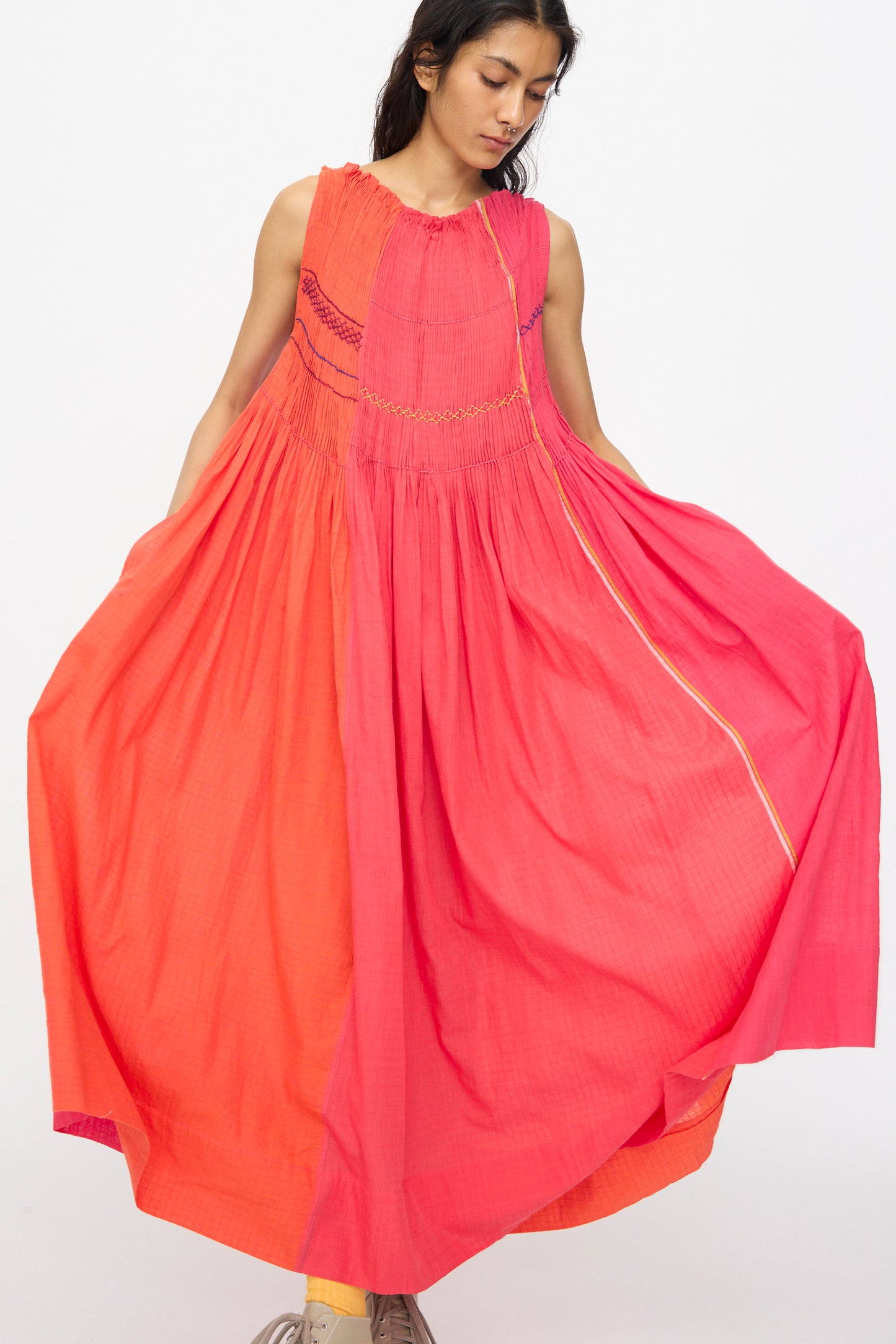 A woman models the Injiri Woven Cotton Dress in Pink and Red, holding out the sides to show its loose, sleeveless design against a plain white background.