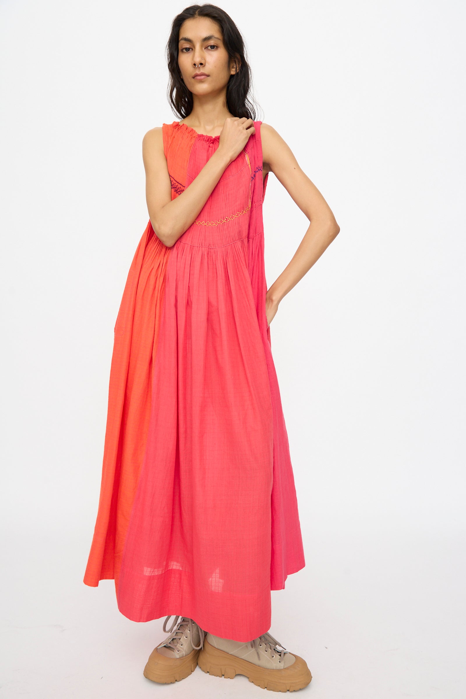 A person poses against a white background wearing the Injiri Woven Cotton Dress in Pink and Red, styled with tan sneakers.