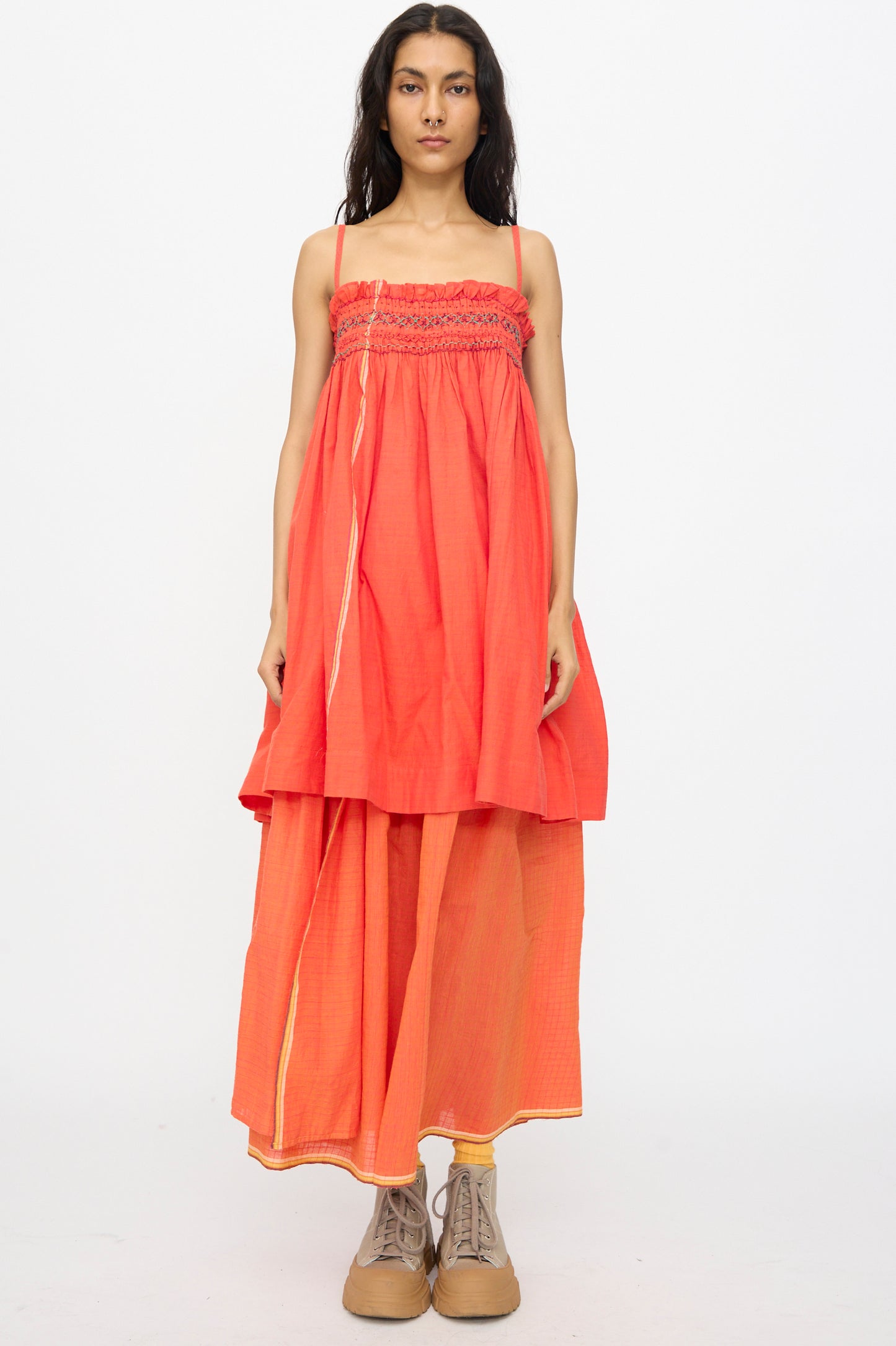 A woman faces forward in the Injiri Woven Cotton Sleeveless Top in Red, featuring an embroidered square neck, styled with wide-legged red pants and tan boots, her expression neutral against a plain white background.