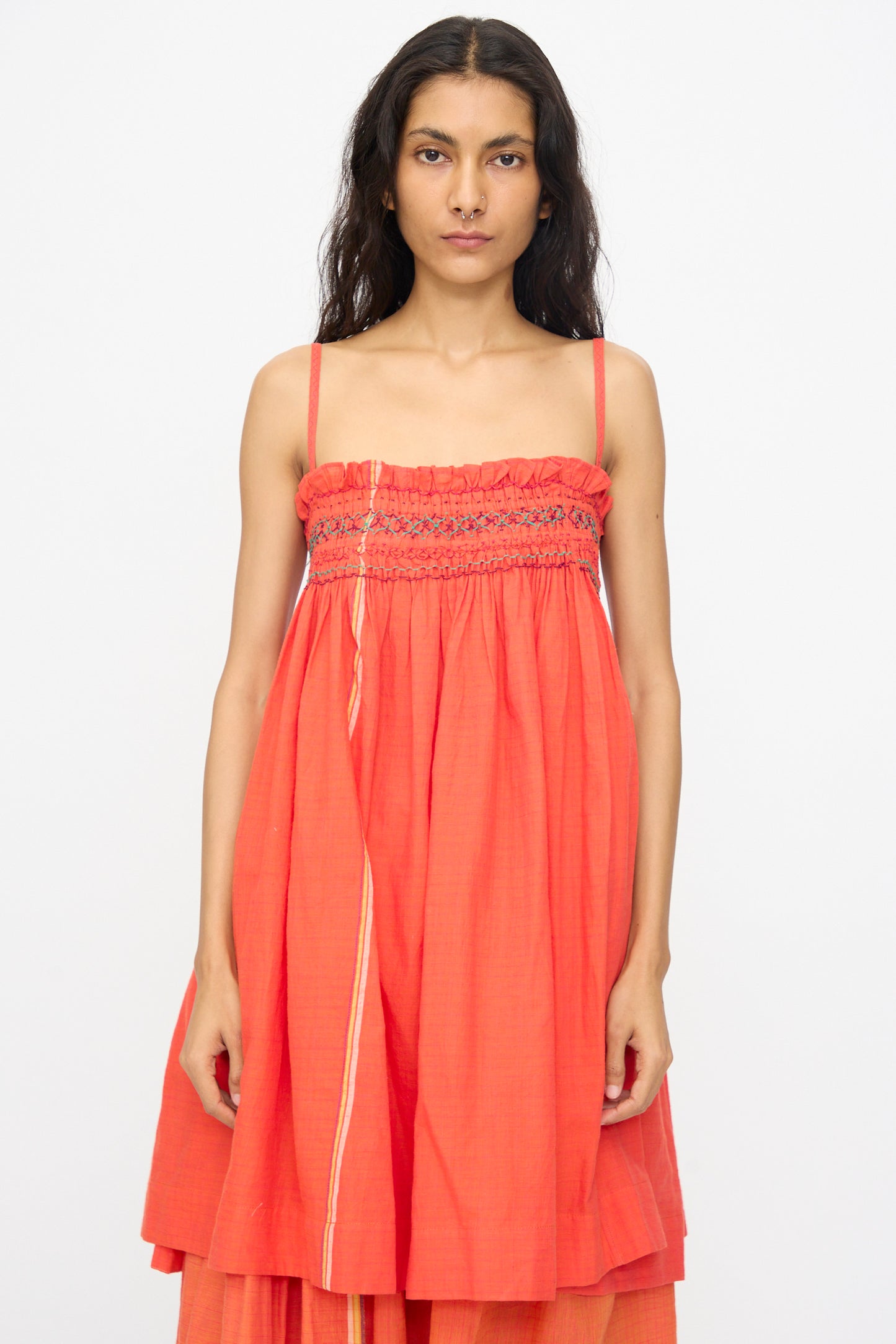 A woman with long dark hair wears the Injiri Woven Cotton Sleeveless Top in Red, featuring spaghetti straps and a smocked bodice, styled as a loose dress against a plain white background.