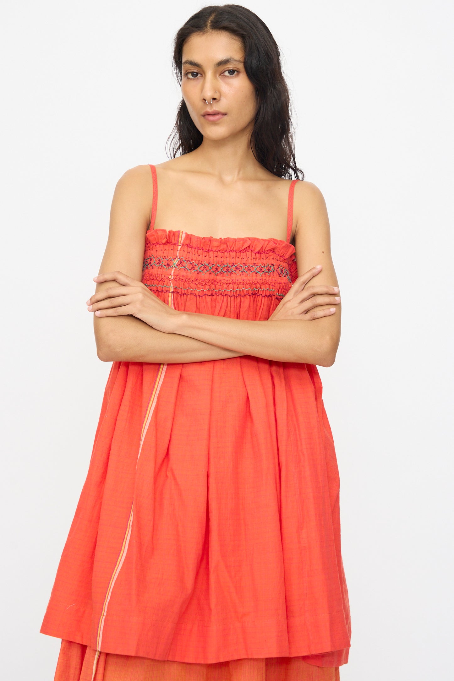 A woman with long hair stands against a white background, arms crossed, wearing the Injiri Woven Cotton Sleeveless Top in Red featuring an embroidered square neck and loose fit.