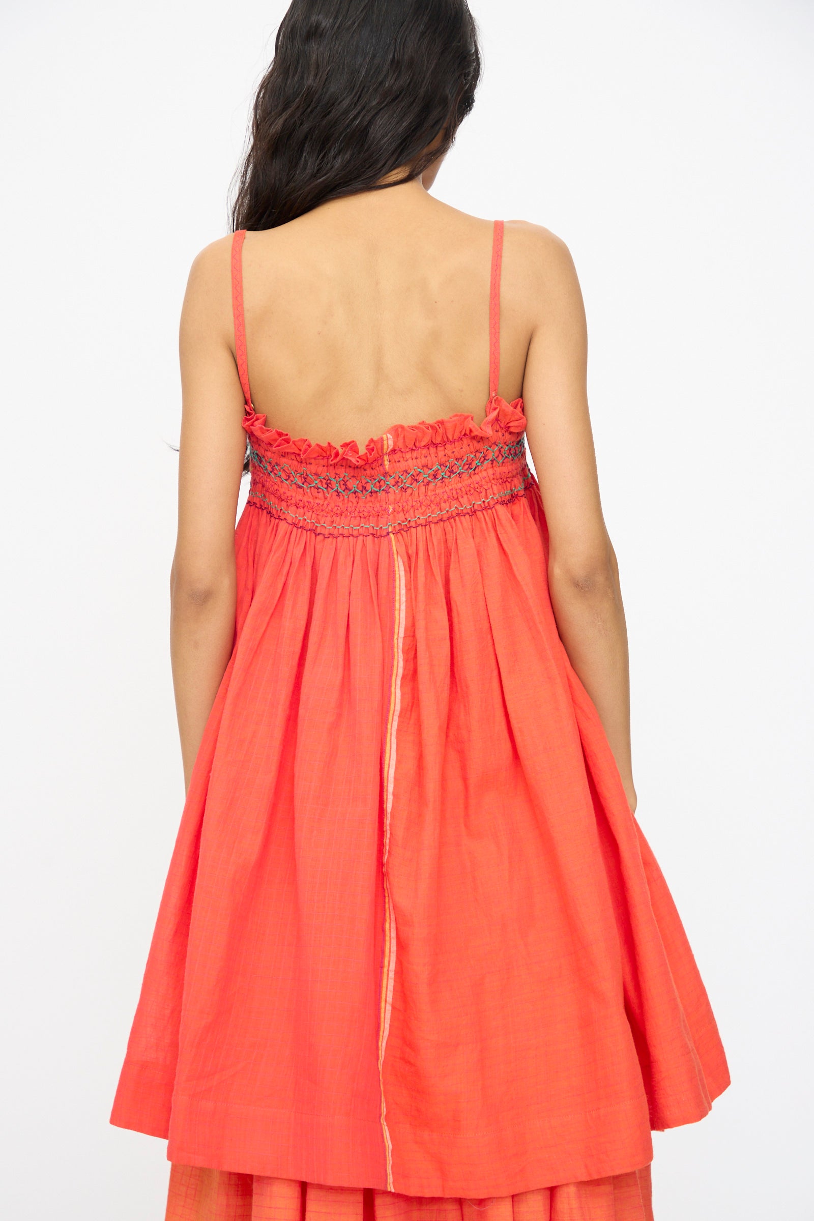 A woman with long dark hair faces away from the camera against a plain white background, wearing Injiri's Woven Cotton Sleeveless Top in Red. The top features a loose fit, embroidered square neck, and smocked upper back detailing.