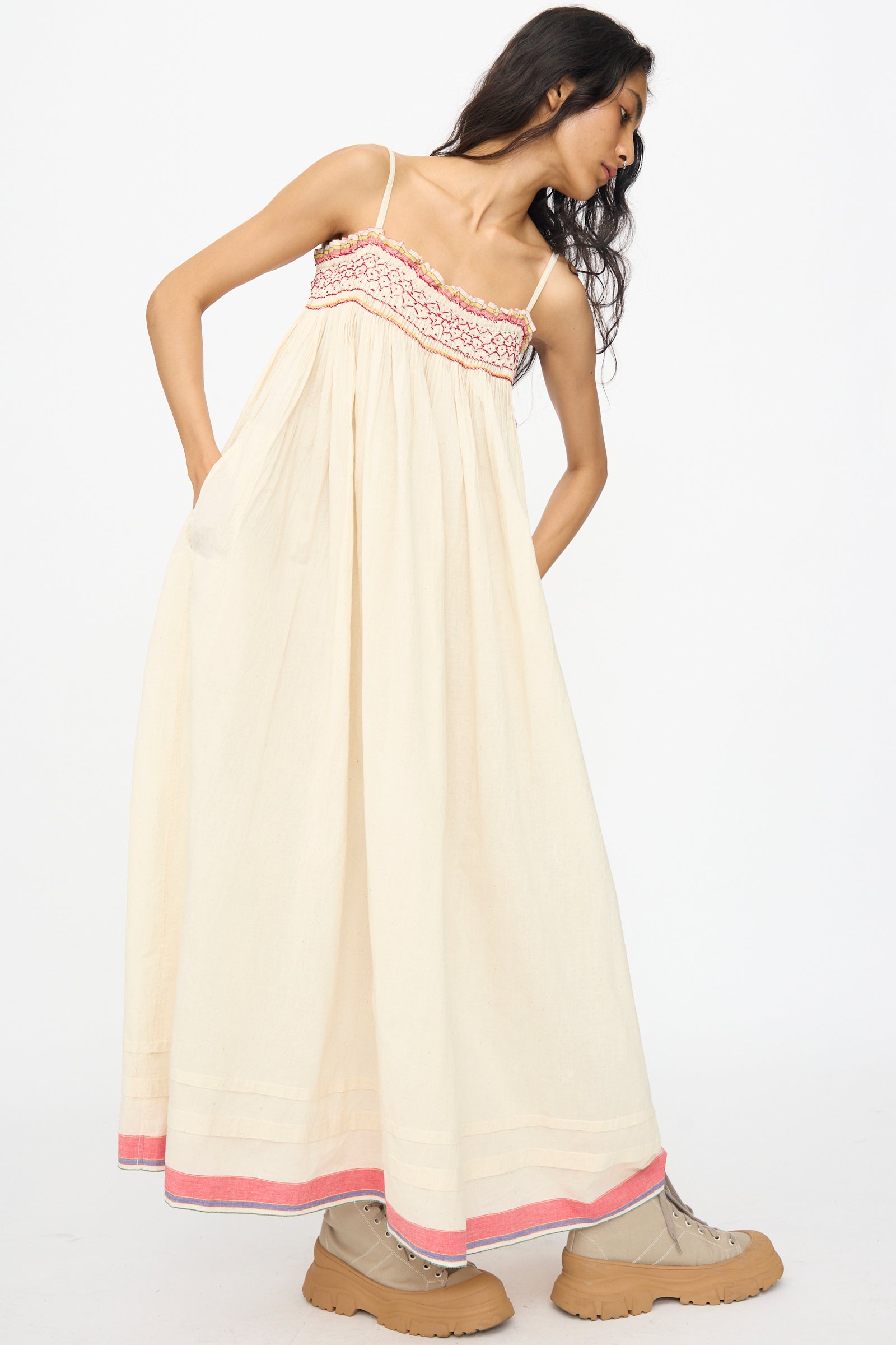 A woman wears the Injiri Woven Cotton Slip Dress in White with Red Stitch and tan boots, posing against a plain white background.