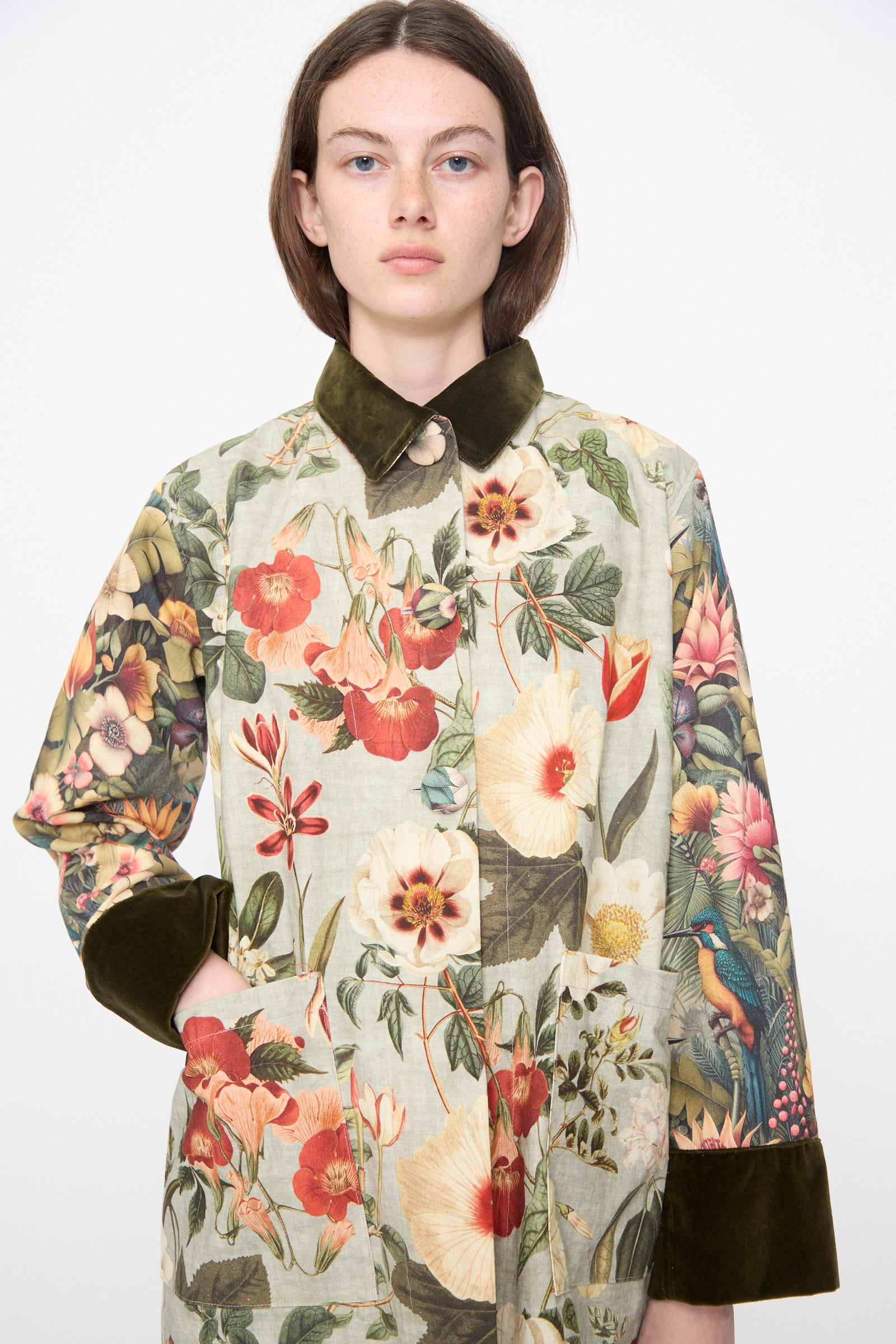 A person models the Intensity Cotton Coat with Velvet in Green Floral, featuring a green velvet collar and cuffs, against a plain white background.