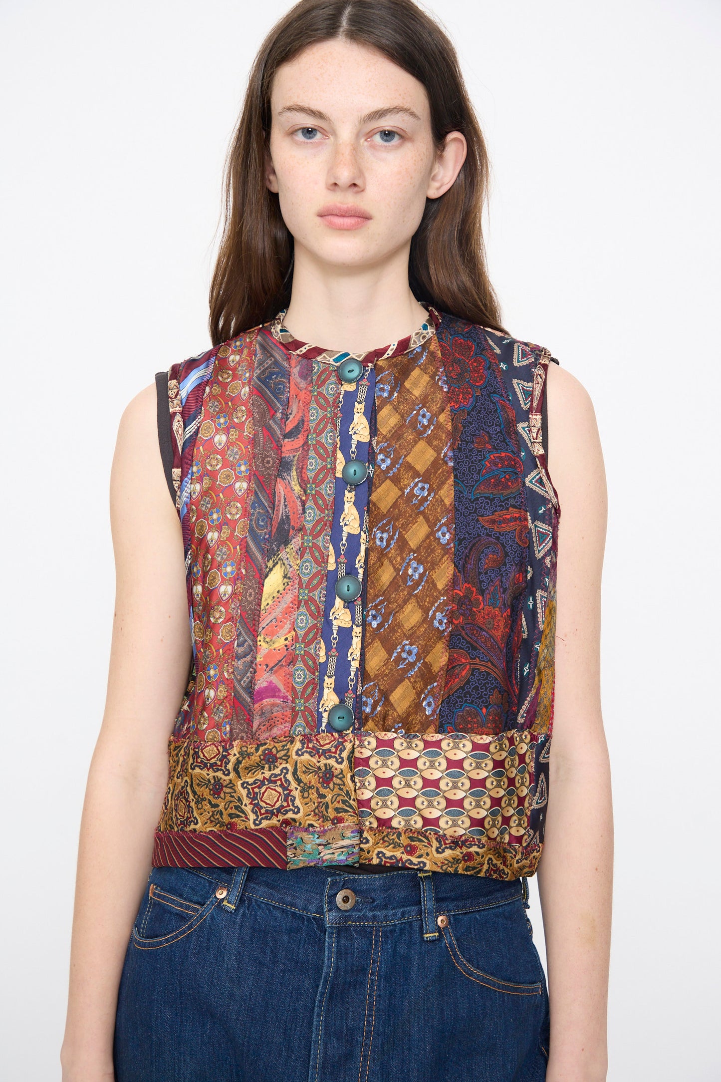 A woman with long brown hair wears the Intensity Ties Vest in Multi— a unique patchwork silk vest—paired with jeans, standing against a plain white background.