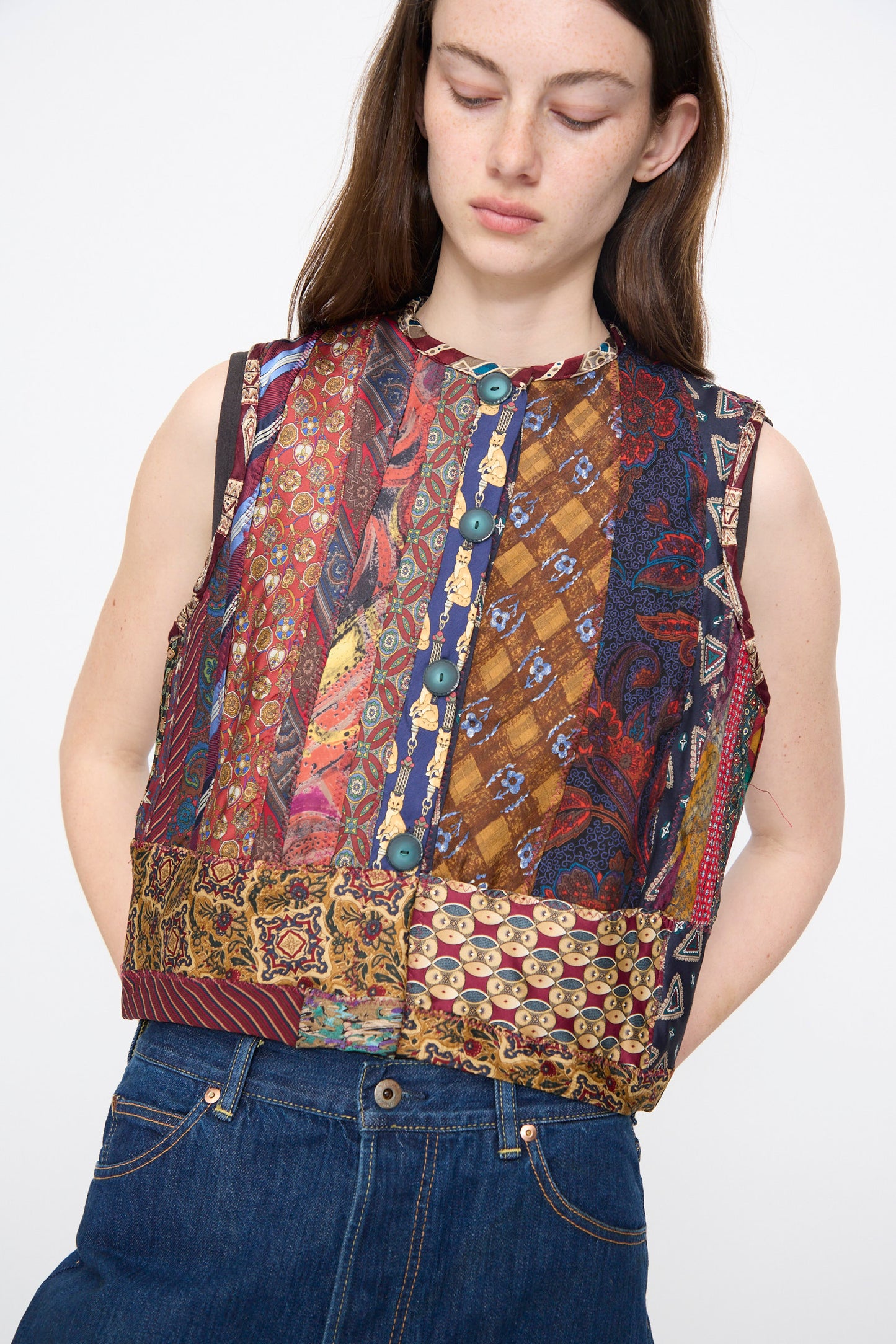 A woman wears Intensity's Ties Vest in Multi—a unique, sleeveless silk piece with blue buttons—paired with blue jeans against a plain background.