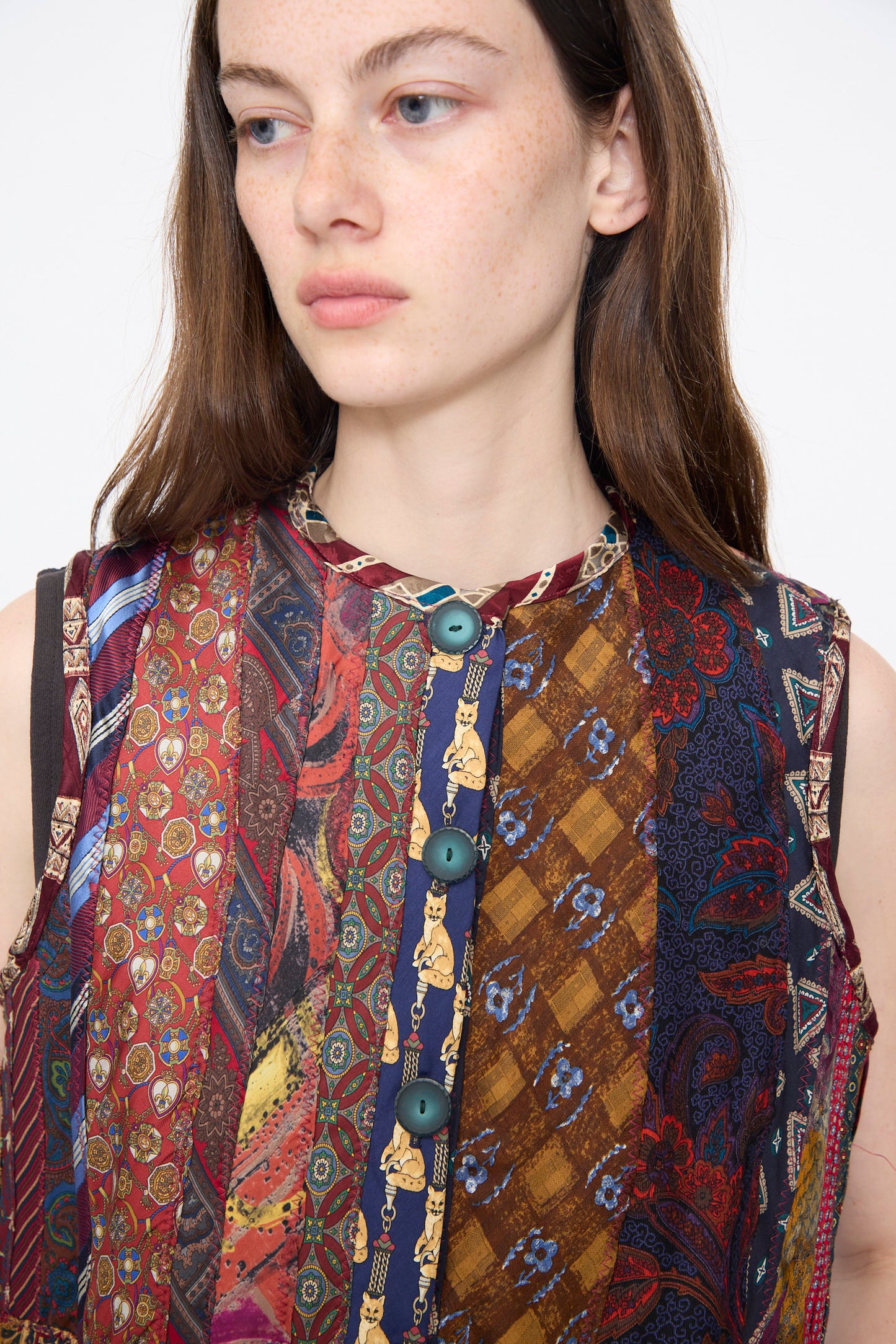 A young woman with long brown hair wears the Intensity Ties Vest in Multi, a unique vintage silk vest featuring a multicolored patchwork pattern and large buttons, posing slightly to the side against a plain background.
