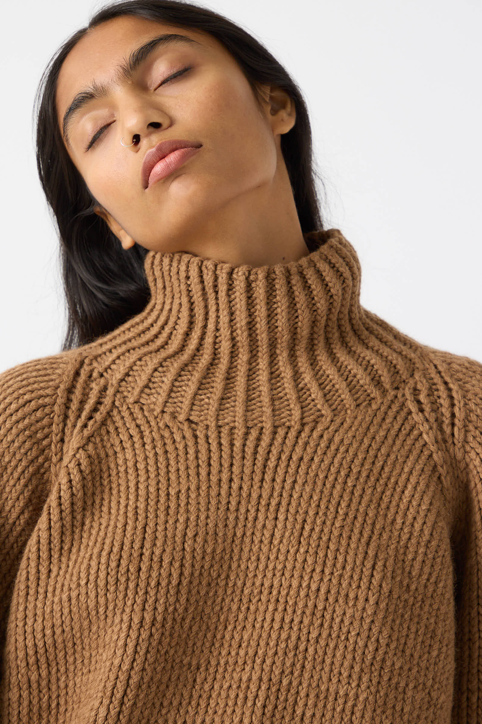 A person with long dark hair and closed eyes is wearing a relaxed fit, chunky Jan-Jan Van Essche Camel Wool Knit Sweater in Natural.