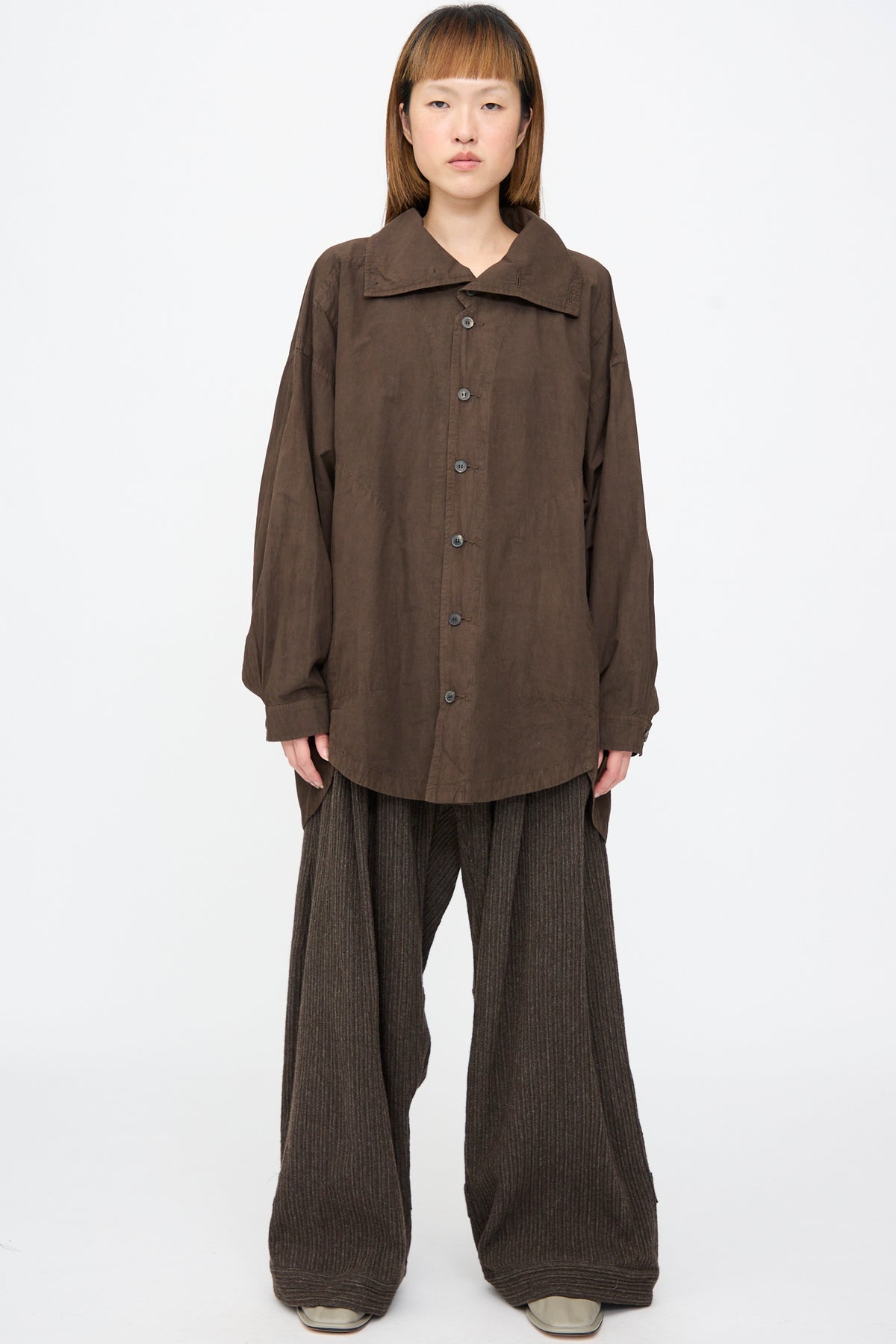 A person wears a dark brown Cotton Wool Shirt #110 in Doro Zome with a wide collar and large buttons, paired with matching wide-leg textured trousers.