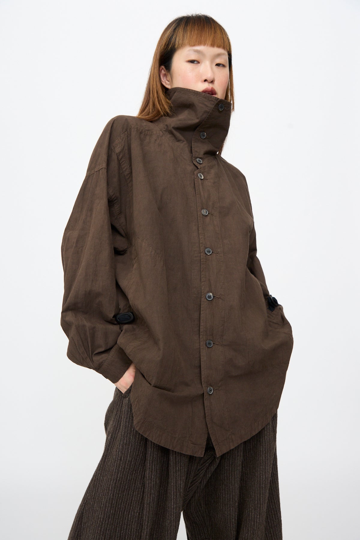 A person wearing a Jan-Jan Van Essche Cotton Wool Shirt #110 in Doro Zome, featuring an oversized fit, high collar, and dropped shoulders, styled with dark pleated trousers.