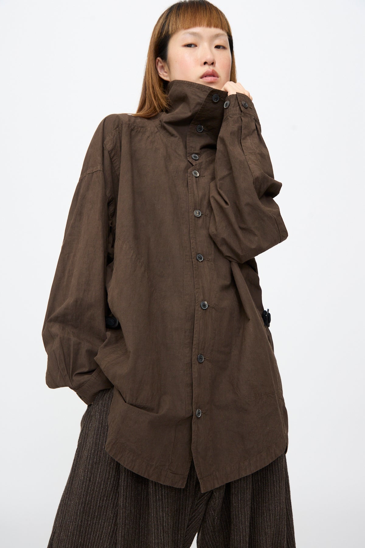 A model wearing the Jan-Jan Van Essche Cotton Wool Shirt #110 in Doro Zome, a brown, cotton-wool blend oversized shirt jacket with a high collar, long sleeves, and side tabs.