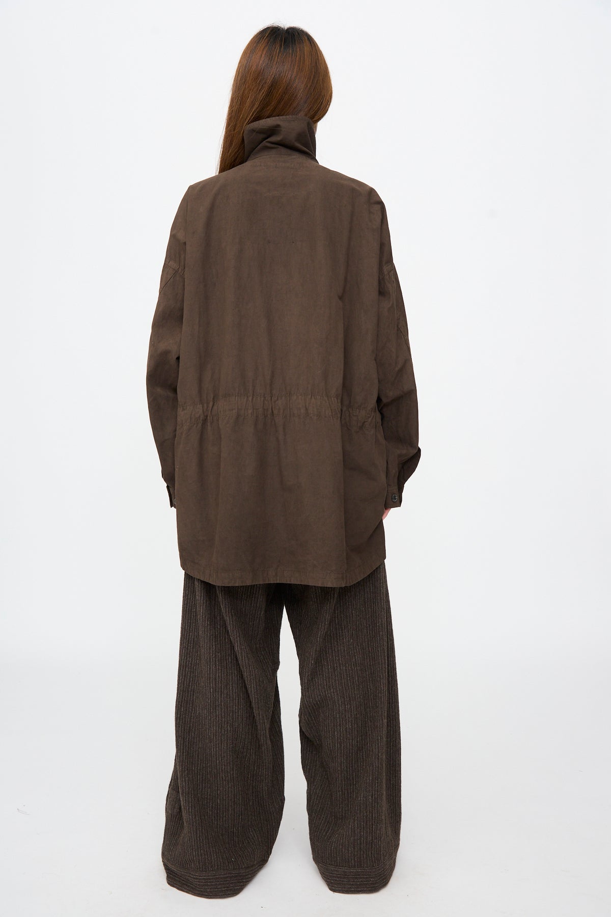 A person seen from behind wears an oversized Cotton Wool Shirt #110 in Doro Zome with a drawstring waist and wide-leg pinstriped trousers.