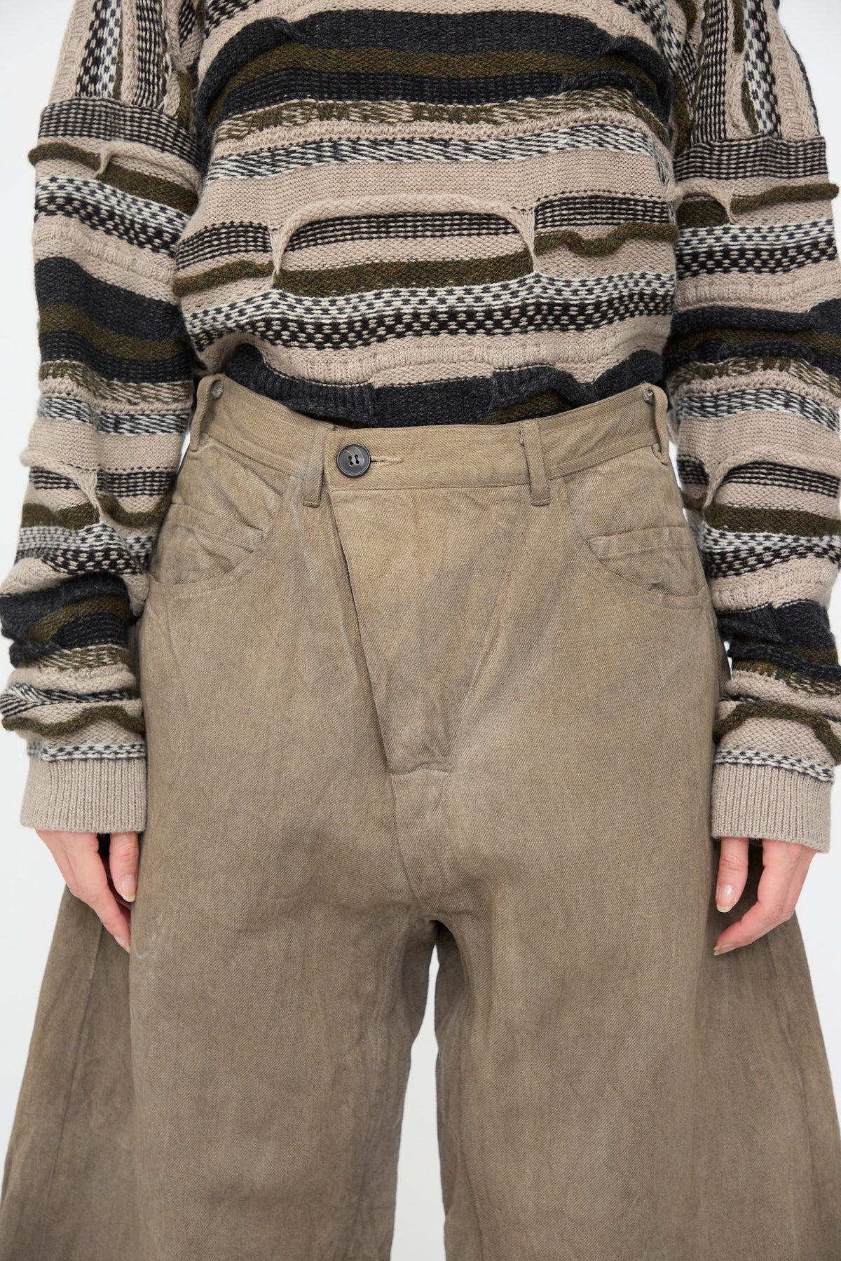 Jan-Jan Van Essche Hemp Bamboo Twill Trousers #90 in Kakishibu and Iron, featuring a taupe wide-leg fit, asymmetric button-fly, and striped knit sweater.