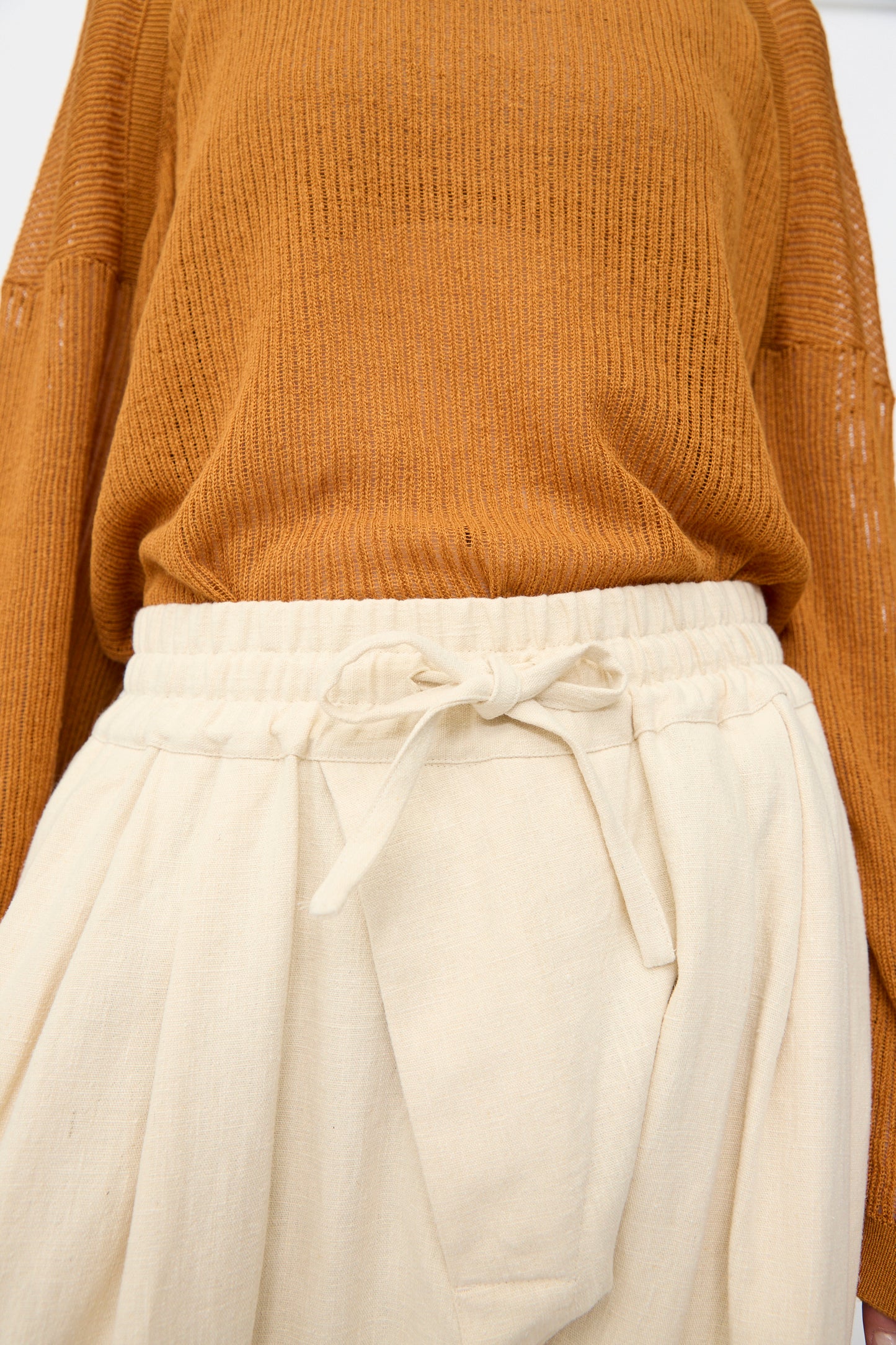A person wearing a brown ribbed sweater and Jan-Jan Van Essche Hemp Soft Canvas Trousers #91 in Kinari, featuring a loose fit, high waist, and elasticated waistband.