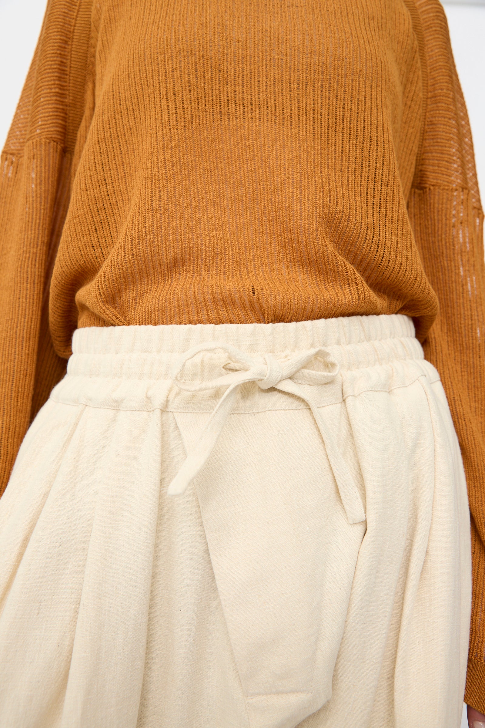 A person wearing a brown ribbed sweater and Jan-Jan Van Essche Hemp Soft Canvas Trousers #91 in Kinari, featuring a loose fit, high waist, and elasticated waistband.
