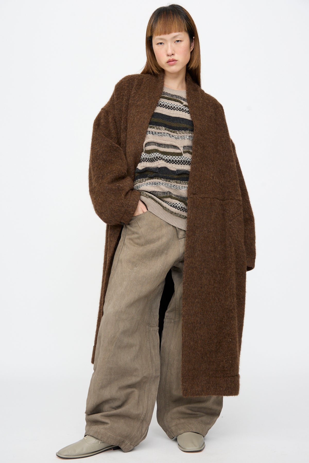 A person wearing a Jan-Jan Van Essche Highpile Herringbone Coat #35 in Brown Alpaca over a textured, patterned sweater and wide-leg trousers.