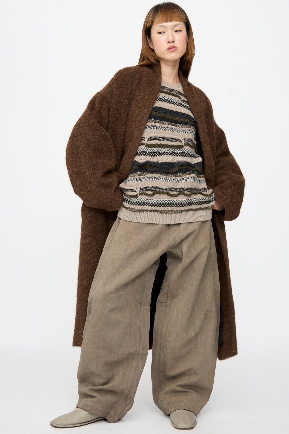 A person wearing a Jan-Jan Van Essche Highpile Herringbone Coat #35 in Brown Alpaca over a patterned sweater and wide-leg trousers.