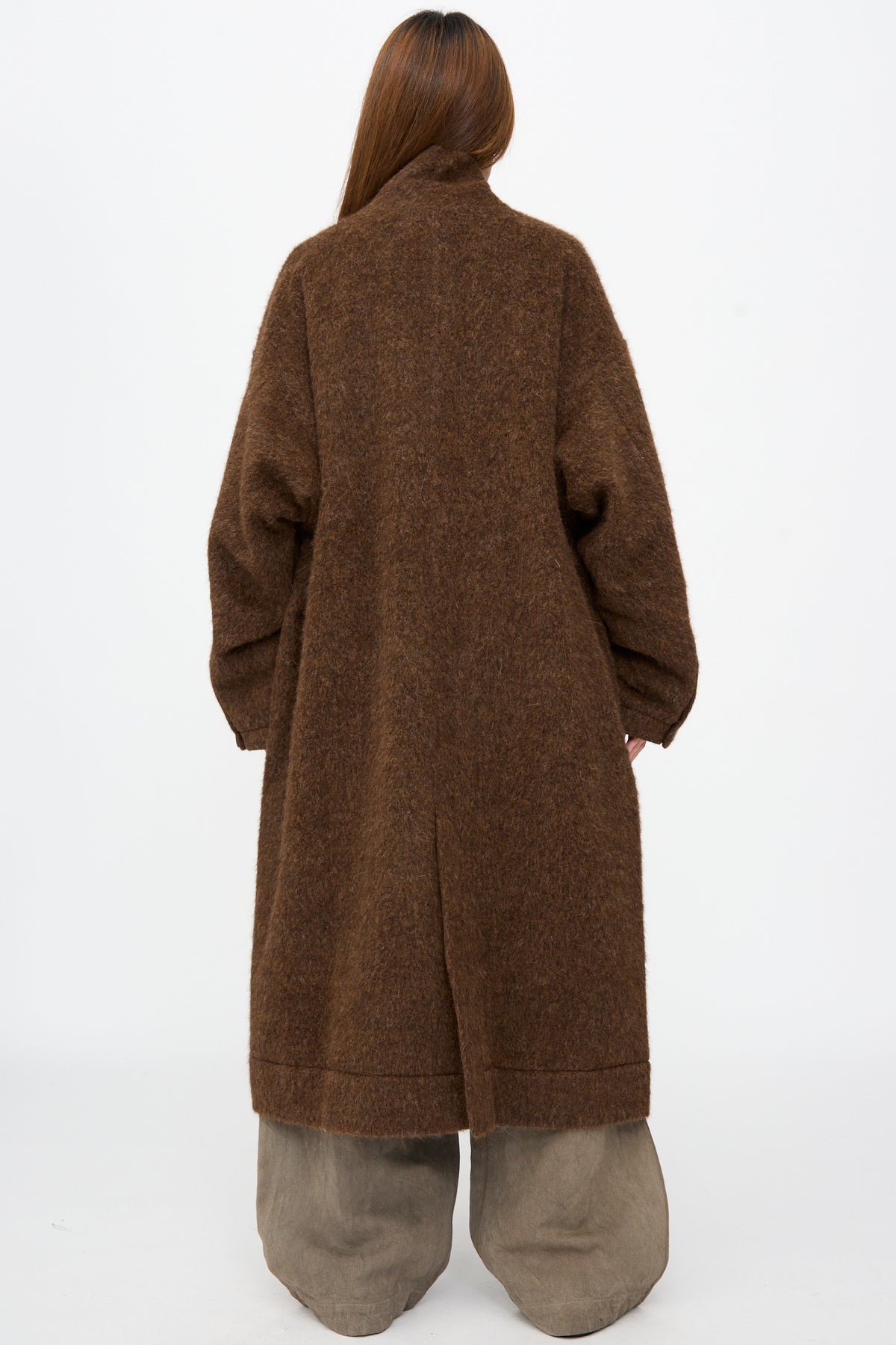 Back view of a person wearing a brown, fuzzy-textured Highpile Herringbone Coat #35 in Brown Alpaca with wide-leg trousers.