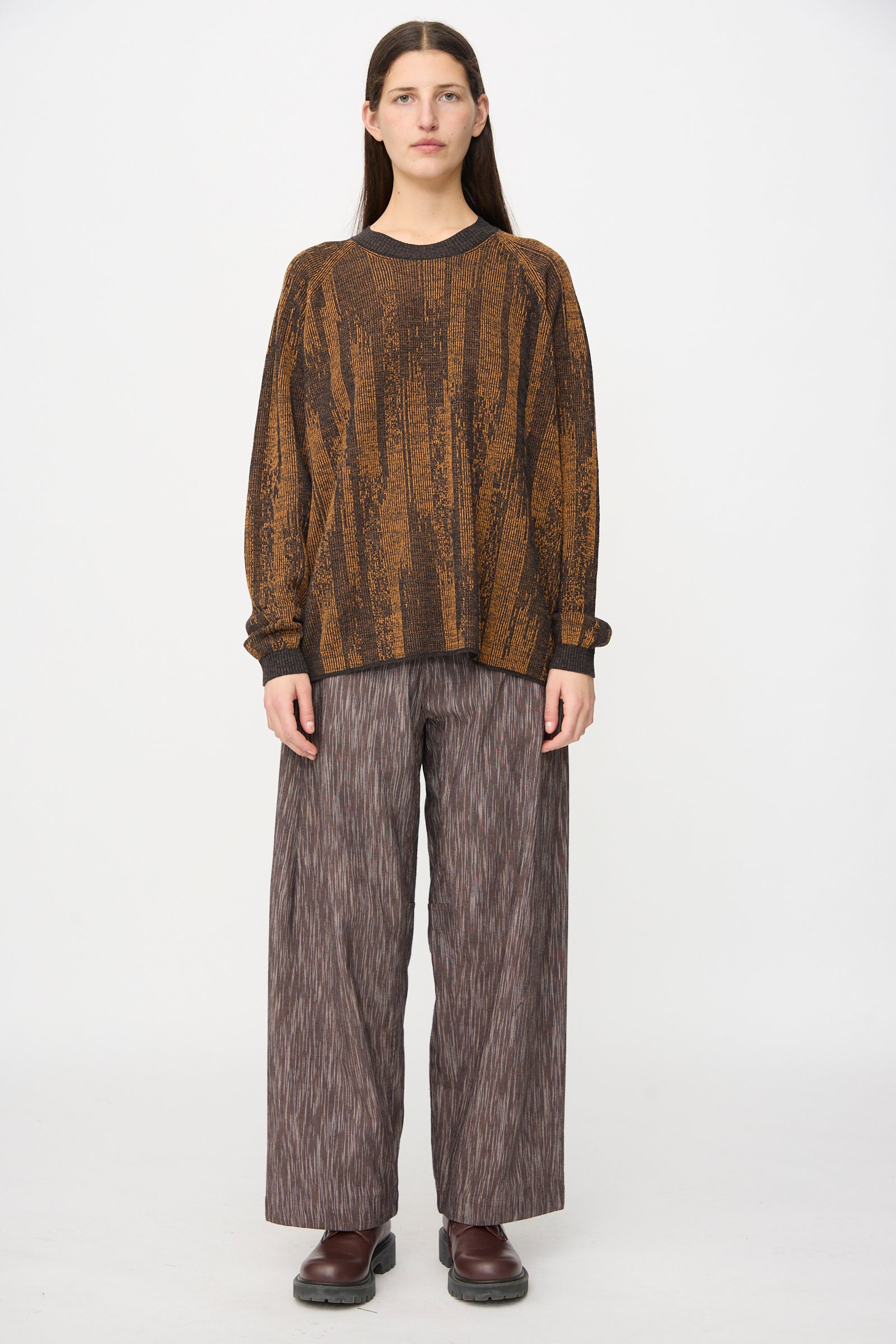 A person stands facing forward against a plain white background, wearing a brown patterned sweater, Jan-Jan Van Essche Kasuri Cotton Silk Trousers #90 in Old Lavender, and dark brown shoes.
