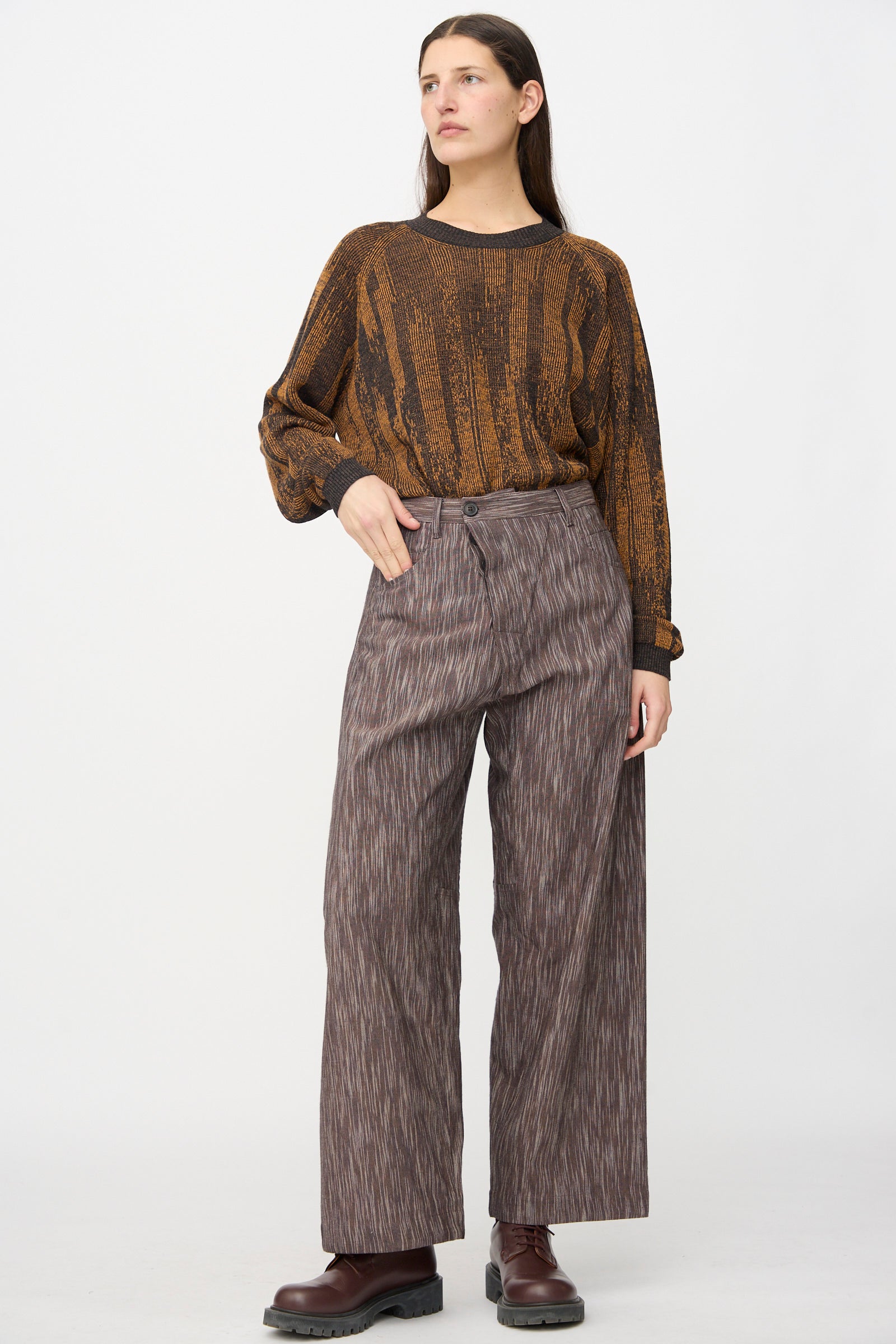 A woman stands against a plain background wearing a brown patterned long-sleeve top, Jan-Jan Van Essche Kasuri Cotton Silk Trousers #90 in Old Lavender, and dark brown shoes.